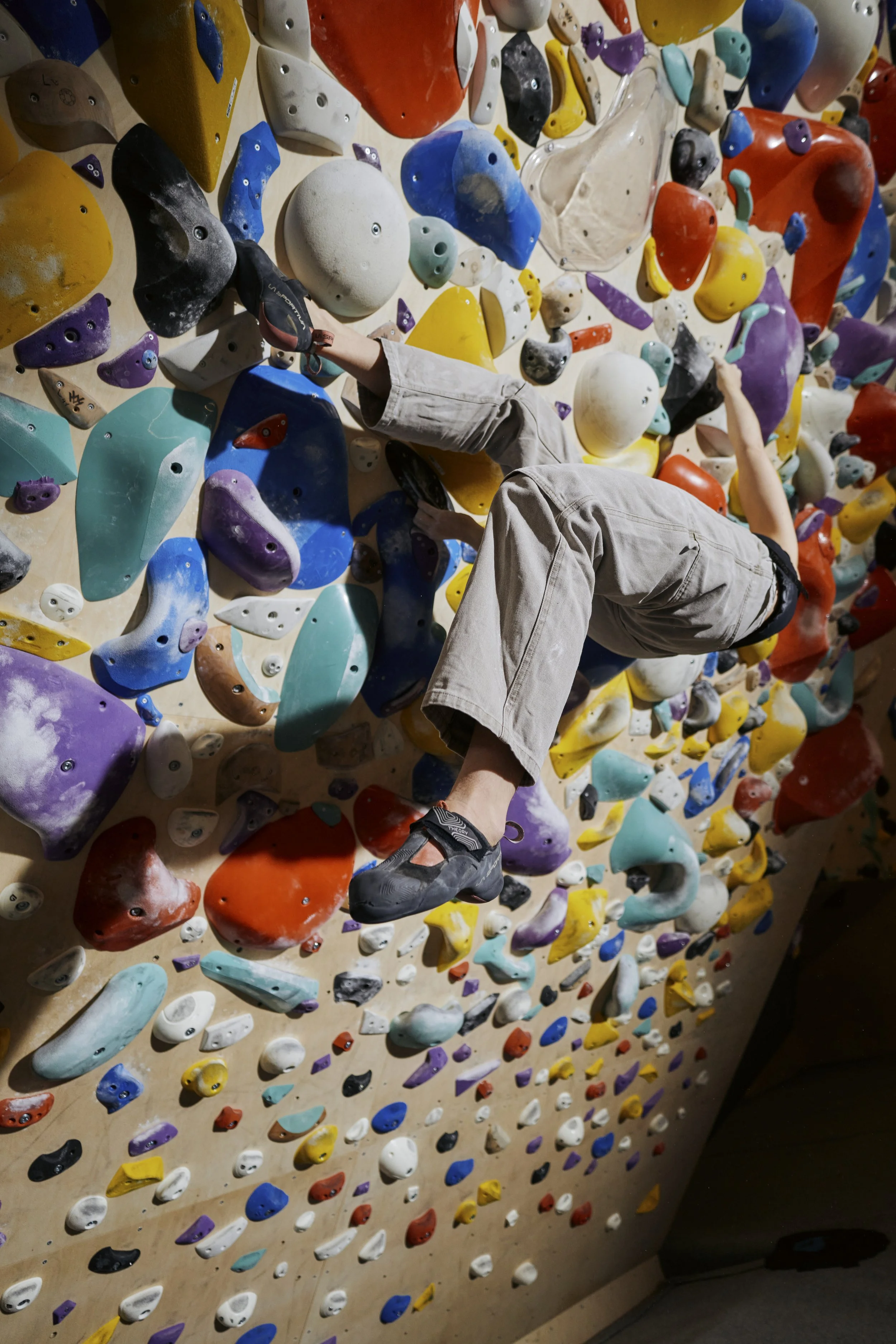 A person climbing an indoor rock climbing wall with colorful holds of various shapes and sizes.