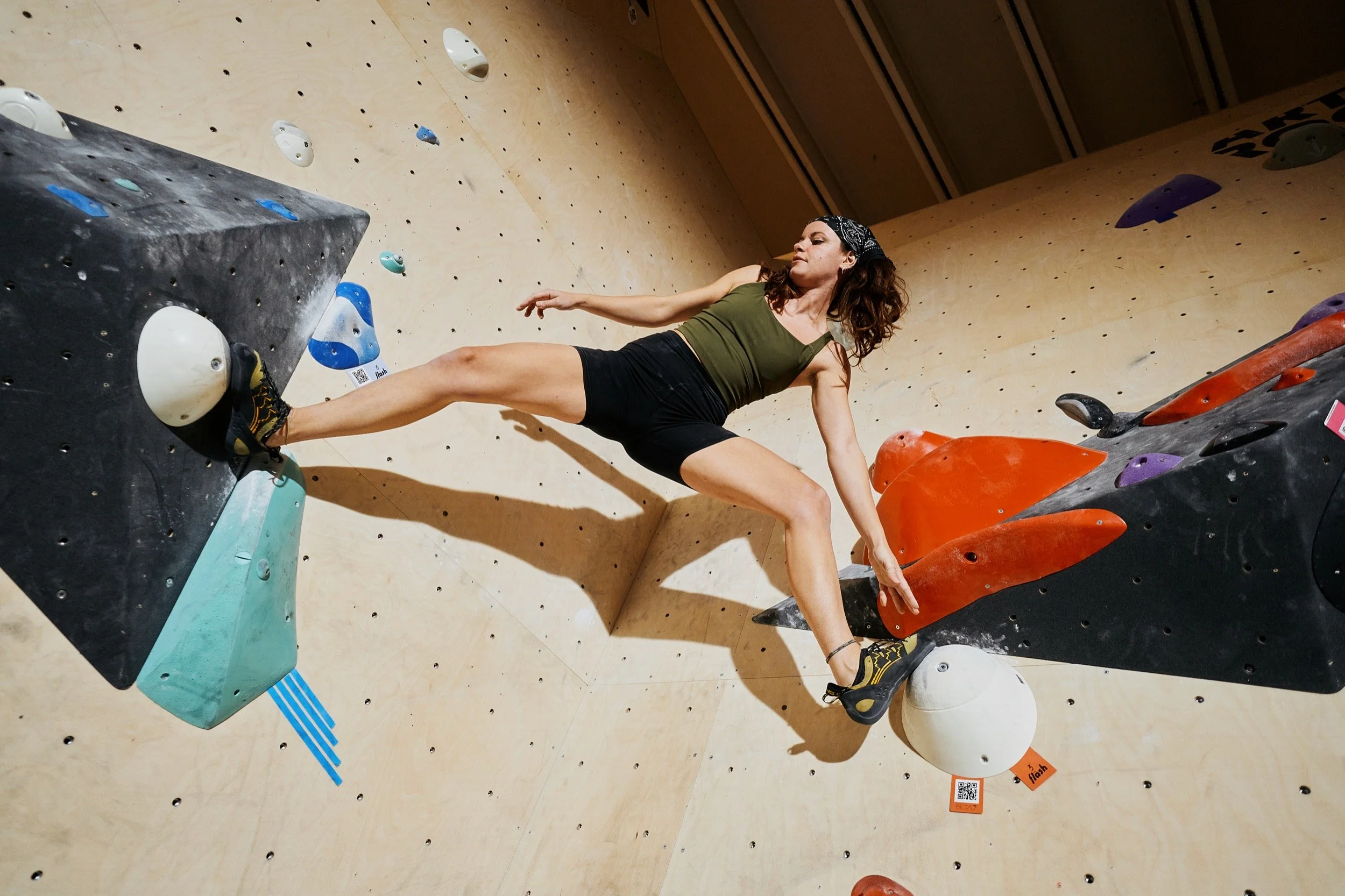 Frau beim Klettern in einer Kletterhalle, die an einer Wand mit künstlichen Griffflächen hoch klettert.