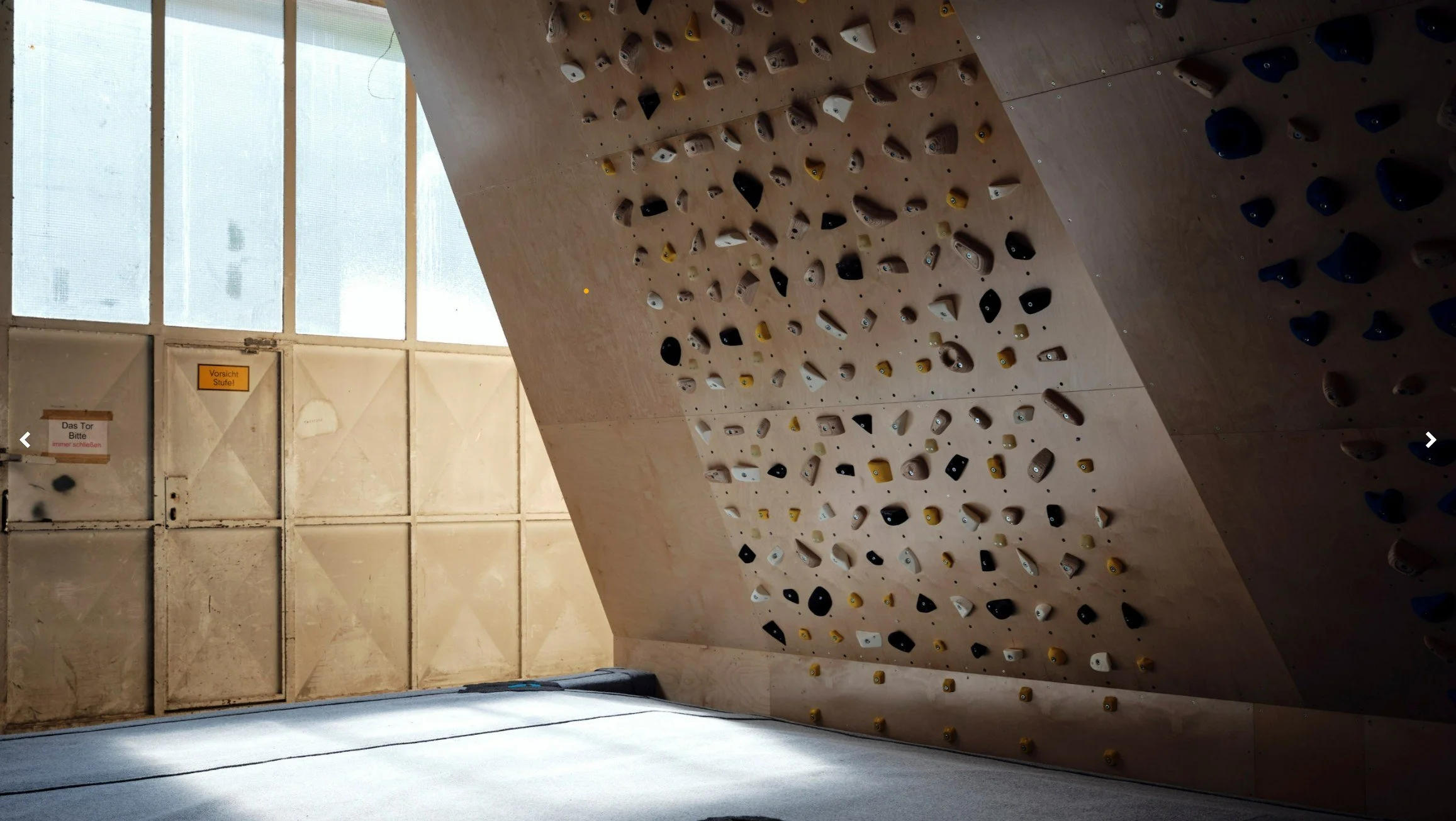 Boulderwand in einem Kletterzentrum mit verschiedenen Griffen, nahe Fenster mit natürlichem Licht.