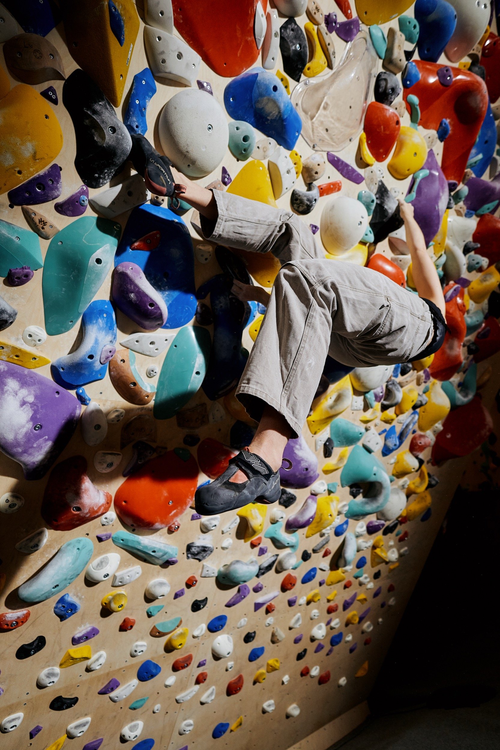 Jemand klettert an einer bunten Kletterwand mit vielen Griffen in verschiedenen Farben.