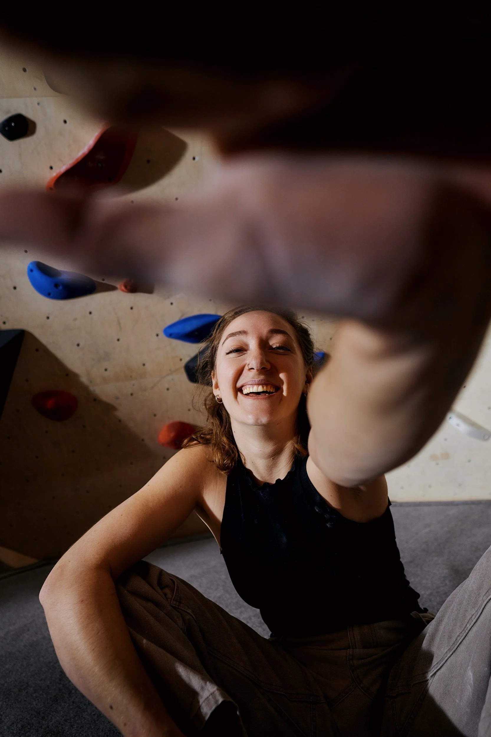 Eine lachende Frau beim Klettern an einer Kletterwand, aufgenommen aus einer unteren Perspektive.