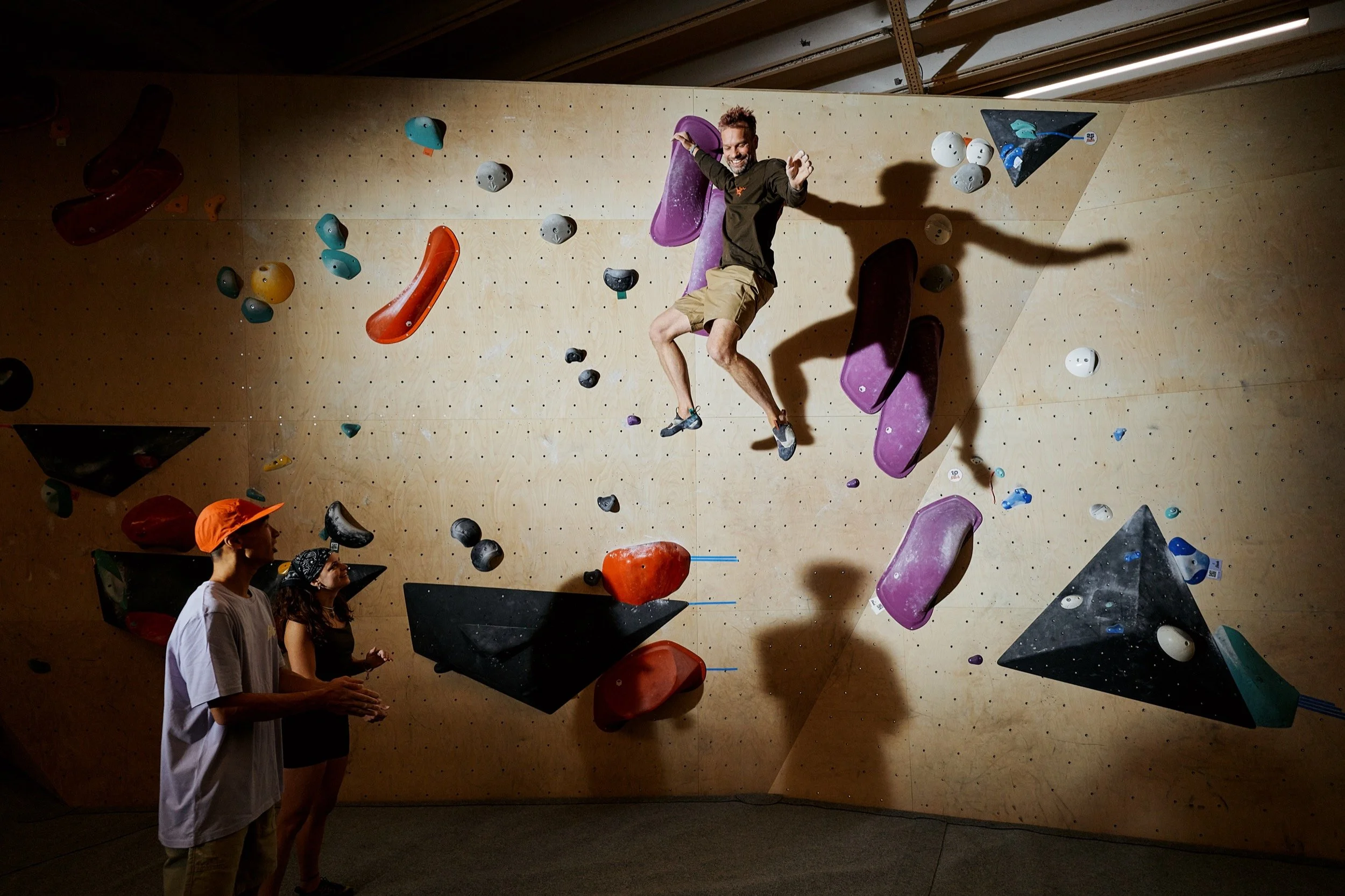 Jemand beim Bouldern in einer Kletterhalle, während zwei Personen zuschauen.