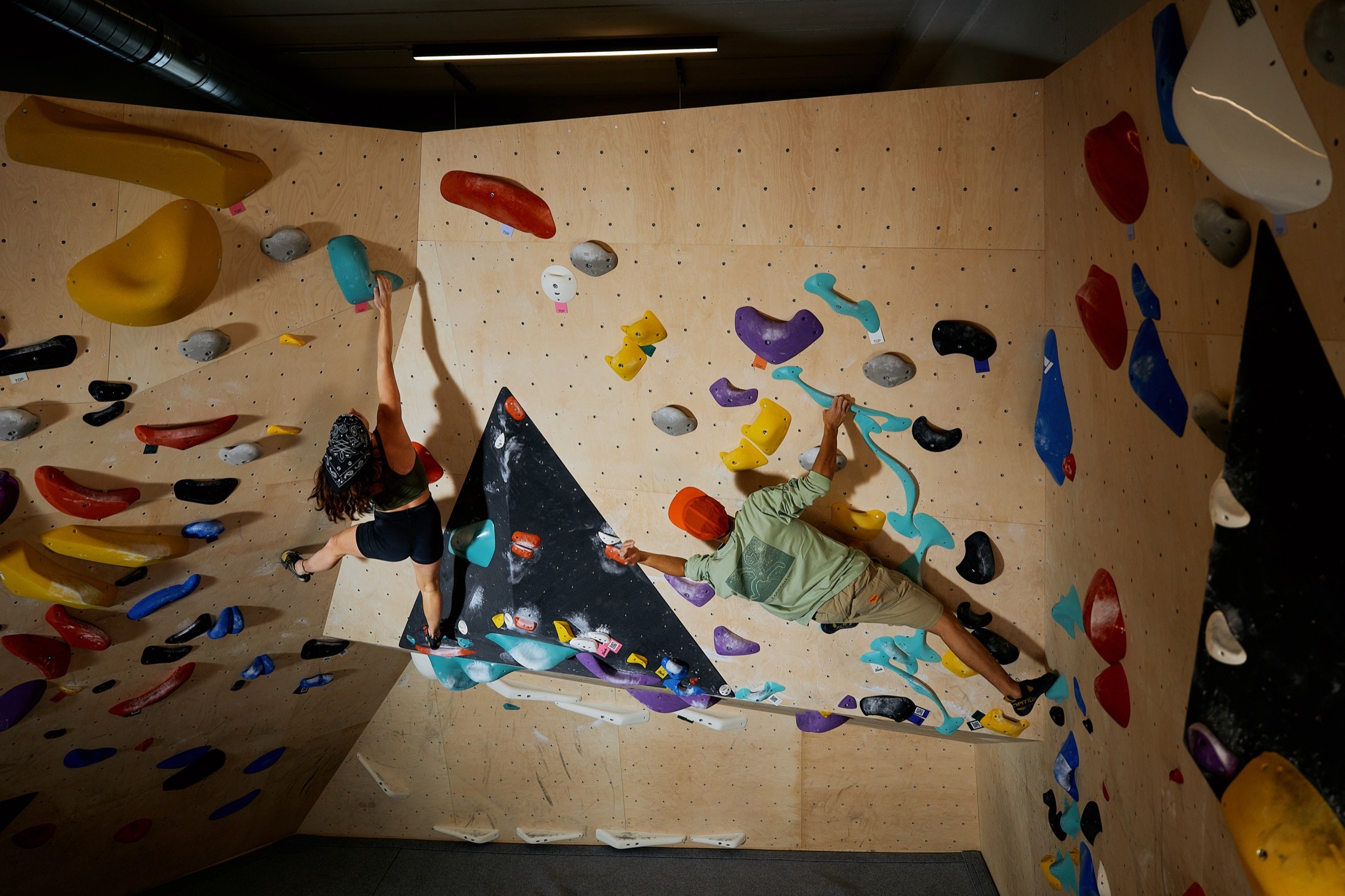 Zwei Kletterer an einer Kletterwand im Indoor-Kletterzentrum, umgeben von bunten Klettergriffen in verschiedenen Formen und Größen.