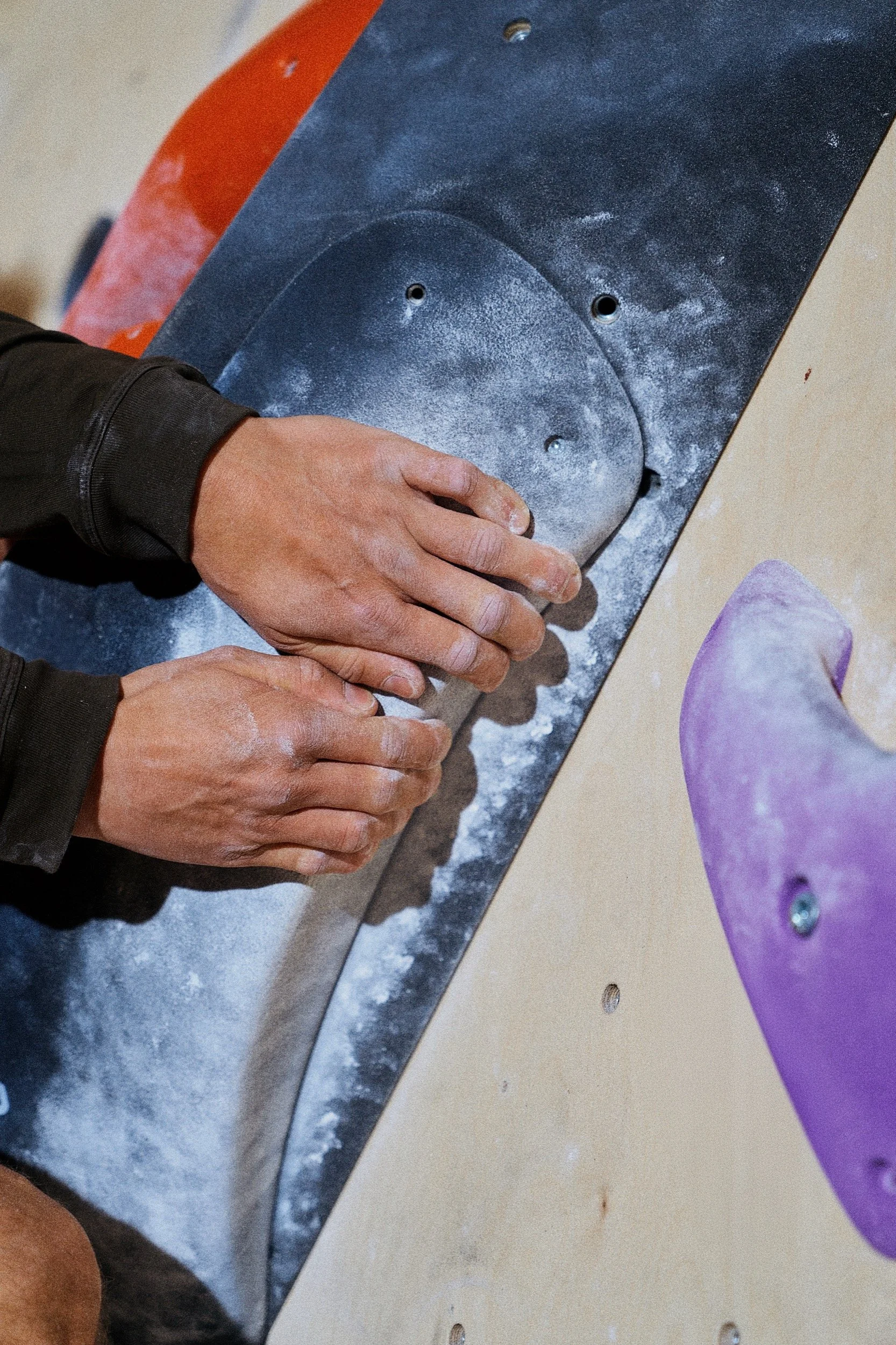 Hand einer Person beim Klettern an einer Kletterwand, die mit farbigen Griffen versehen ist.