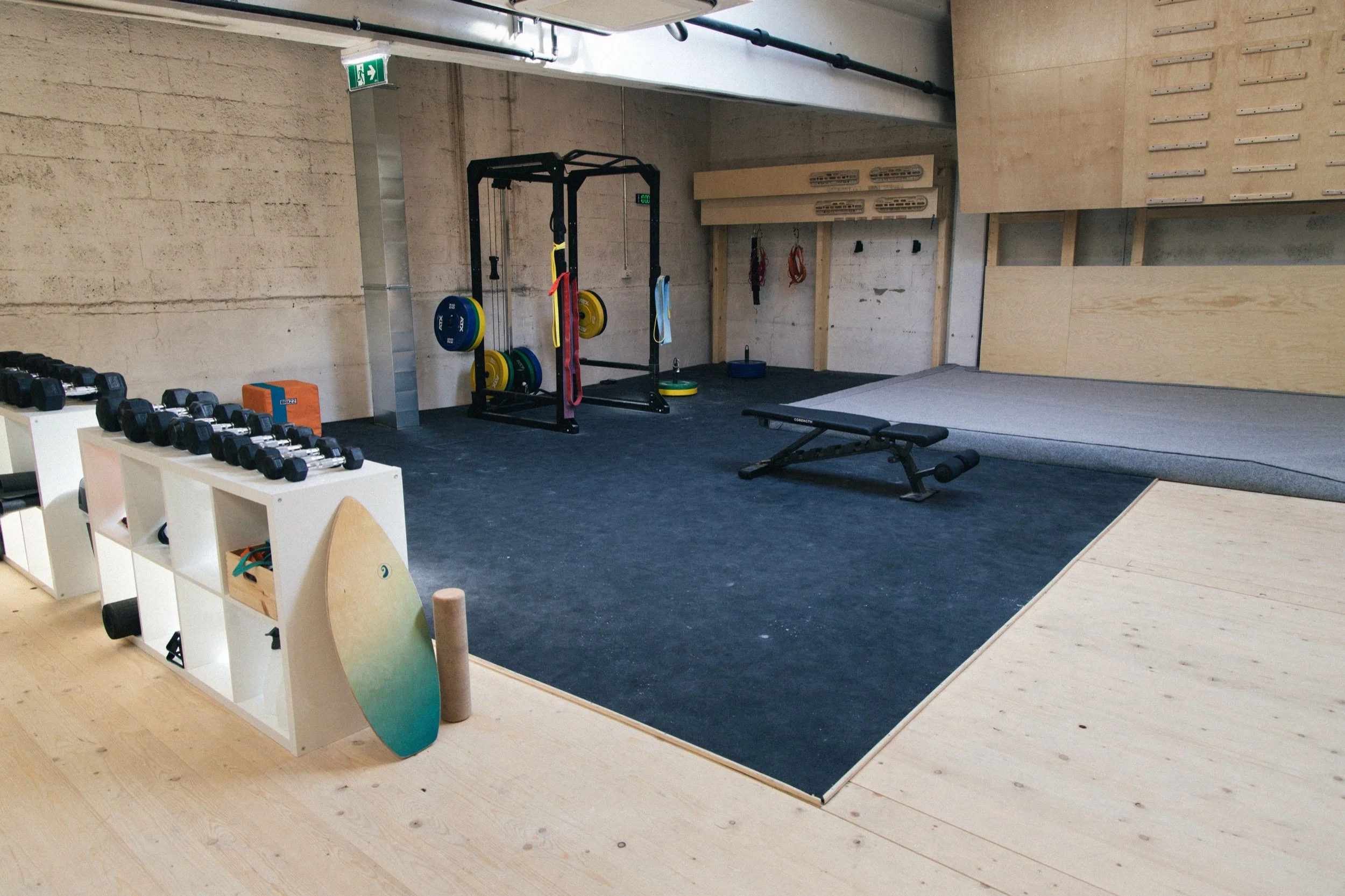 Ein Fitnessraum mit Hanteln, einer Kraftstation, einem Gymnastikball, einem Hocker und einem Mattenbereich.