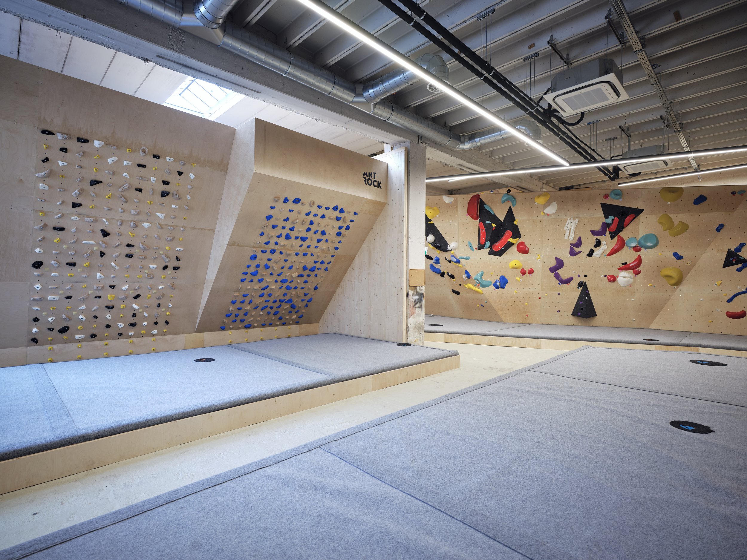 Indoor Kletterhalle mit Kletterwänden in verschiedenen Farben und Schwierigkeitsgraden, mit weichen Matten zum Abspringen und Klettern.