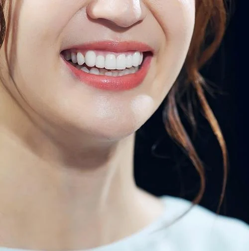 Close-up of a woman's smiling mouth showing white teeth and pink lipstick.