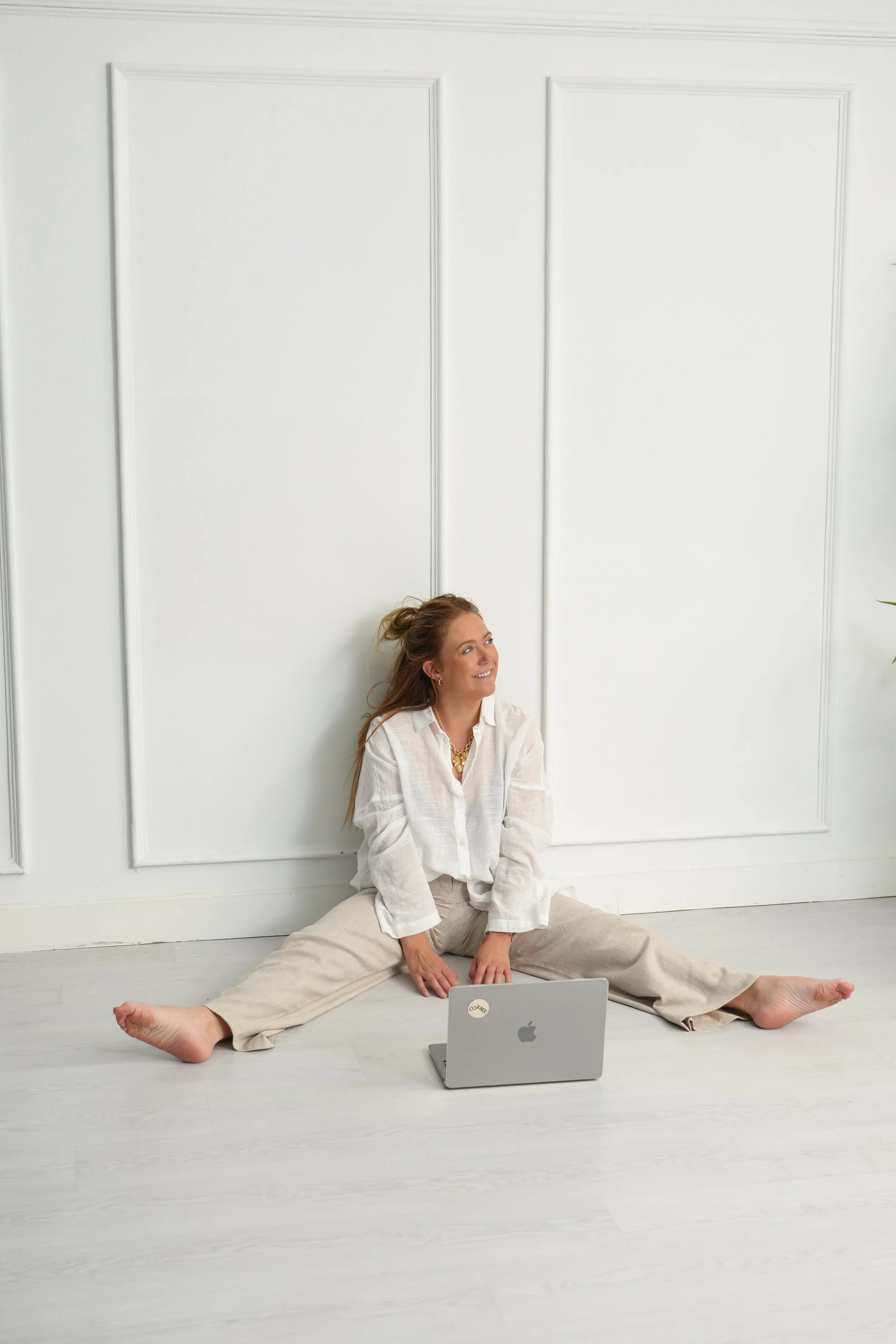 Dona asseguda a terra amb les cames separades davant d'una paret blanca, somrient i mirant cap a un costat, amb un ordinador portàtil davant.