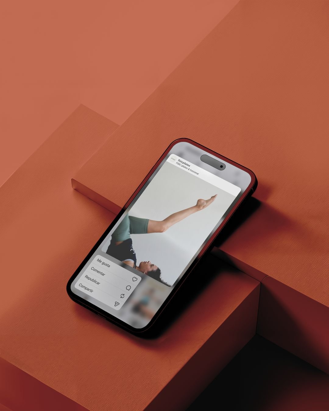 Telèfon intel·ligent recolzat sobre una superfície taronja que mostra una publicació a les xarxes socials d'una persona fent una postura de ioga amb opcions per indicar que t'agrada, comentar, compartir i desar.