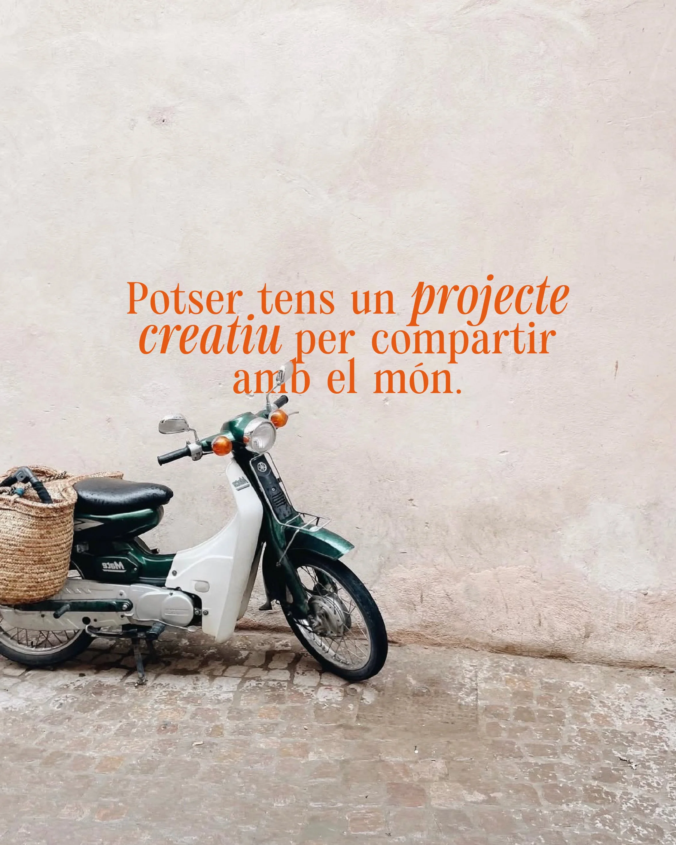 Una moto amb una cistella teixida enganxada a la part posterior, aparcat contra una paret desgastada, amb una cita en català superposada que promou tenir un projecte creatiu per compartir amb el món.