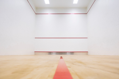 Indoor squash court with white walls, red lines, and wooden floor