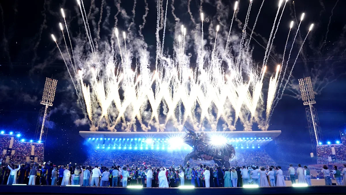 A large crowd at a stadium watching Olympic fireworks light up the Birmingham Olympics night sky.