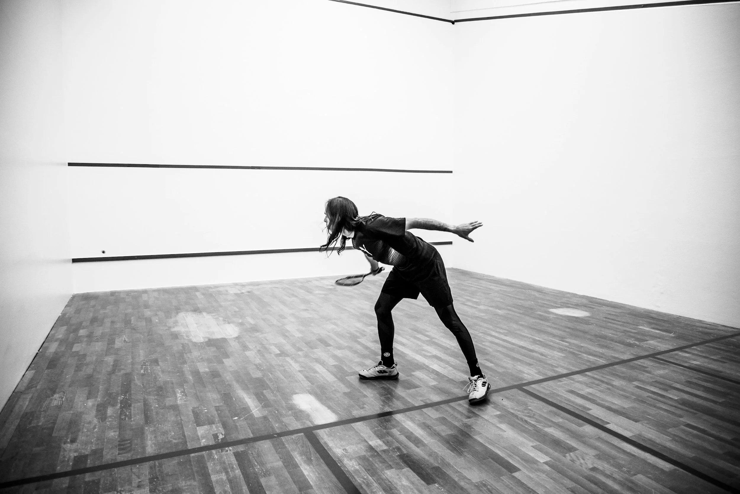 Person playing squash on indoor court, captured in black and white.