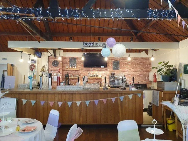 Interior of a decorated event wedding, birthday, family celebration venue with a bar area, hanging paper lanterns, string lights, bunting, and tables set for a celebration.