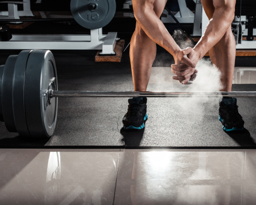 Person in workout clothes lifting a heavy barbell in the gym, with chalk dust rising from their hands.