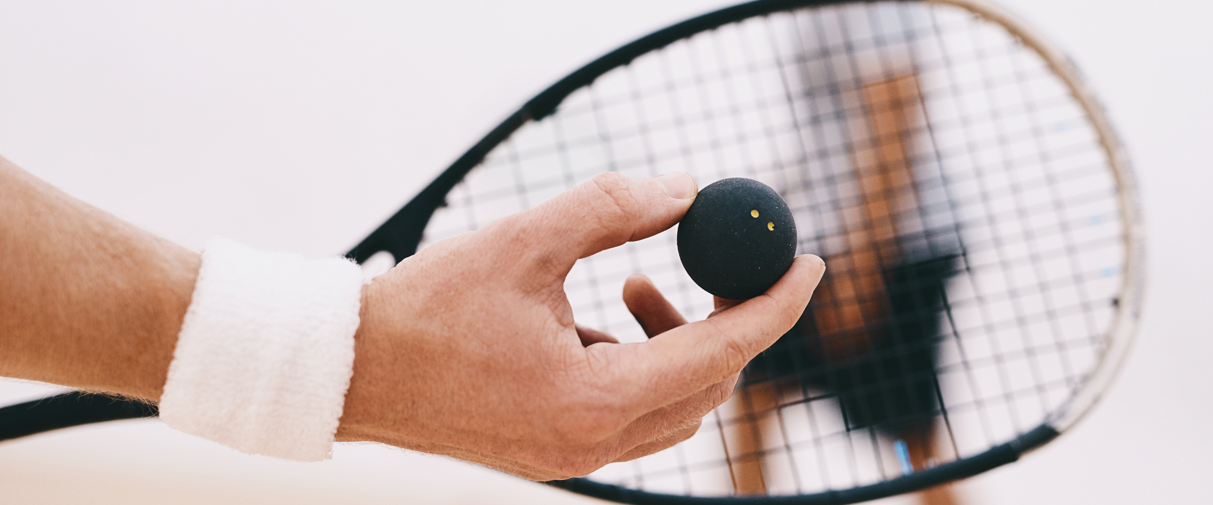 Person holding a black squash ball near a squash racket.
