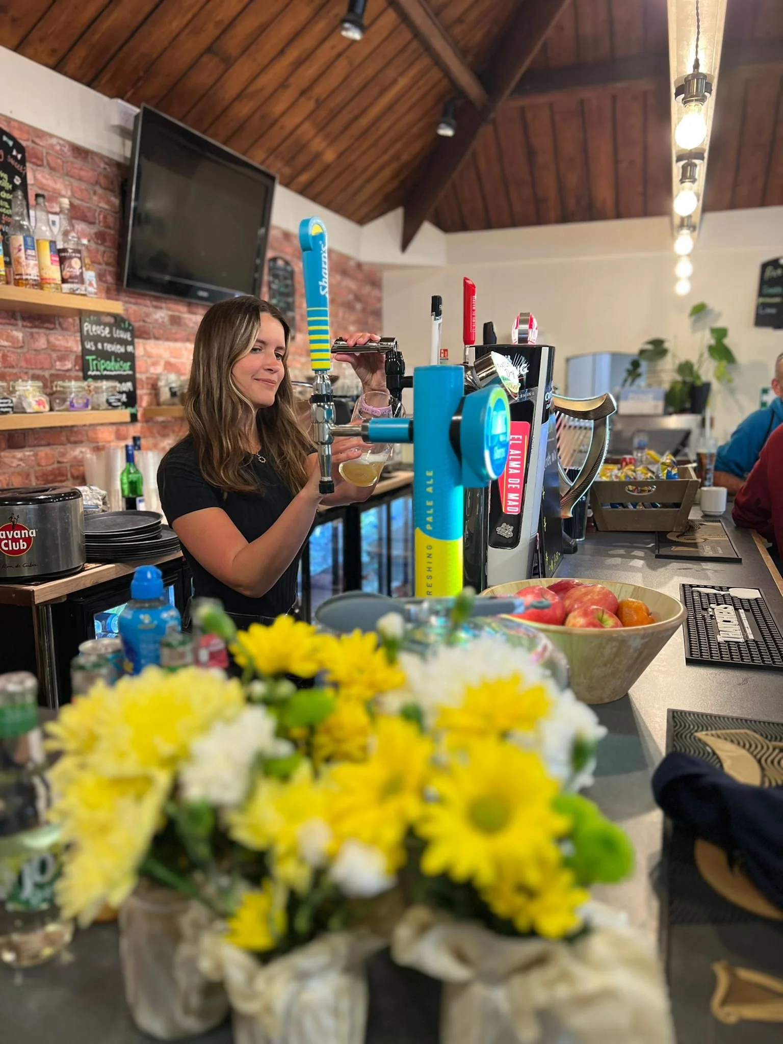 Bartender pouring a drink at a bar with a flower arrangement in the foreground.