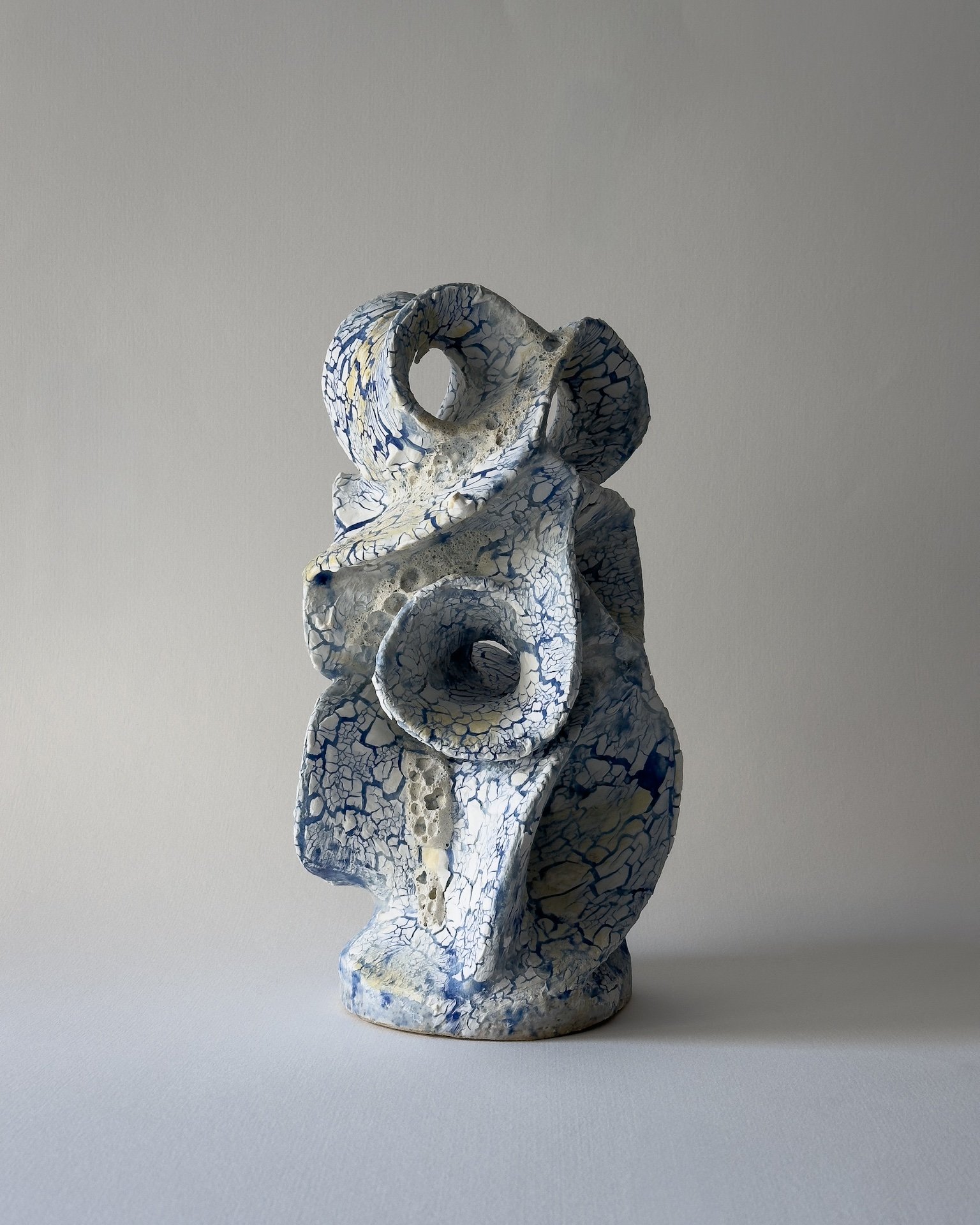 Ceramic sculpture with a textured crackled surface in white and blue, featuring abstract, intertwined, hollow shapes.