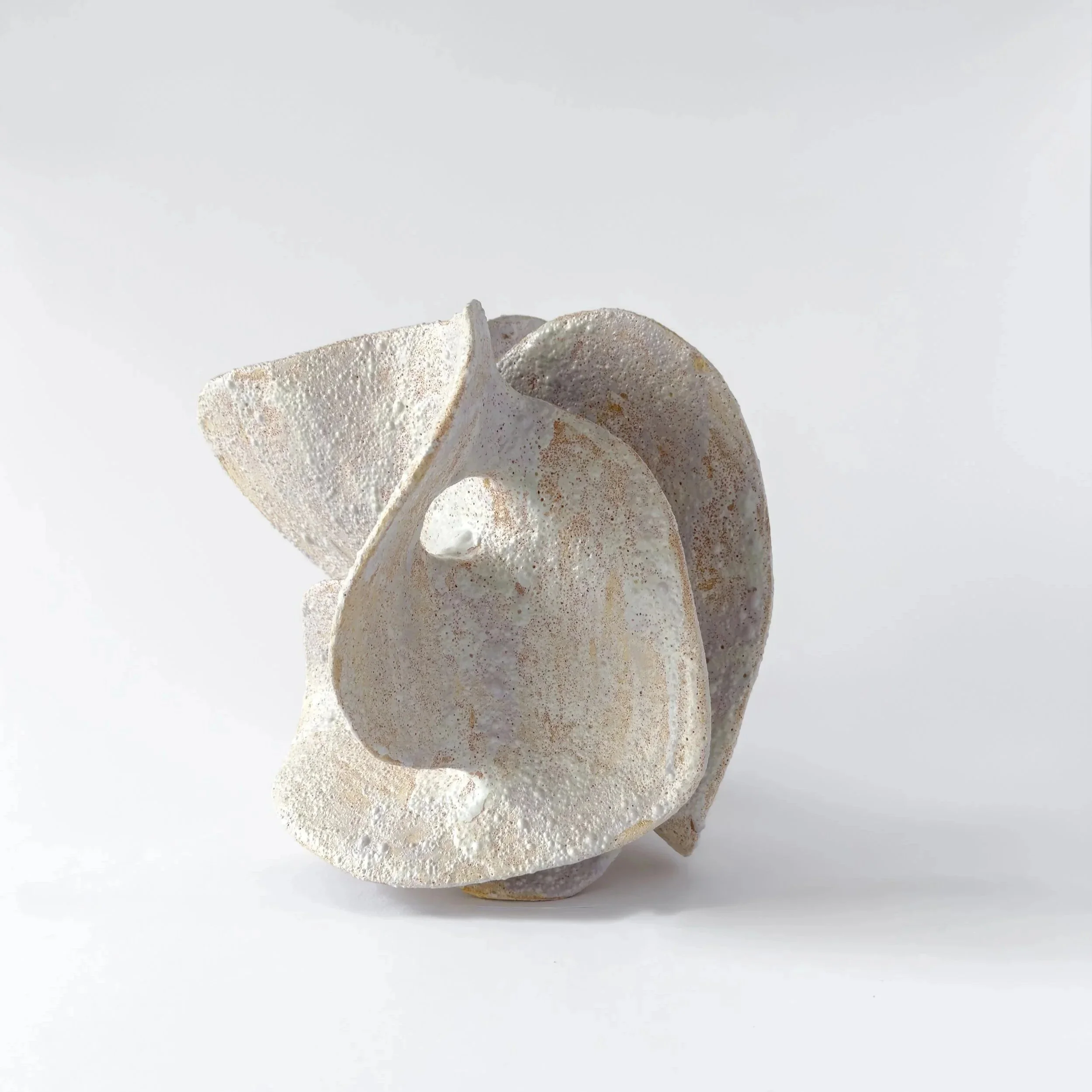 Abstract ceramic sculpture with curved, textured surfaces in light and neutral tones, isolated on a plain white background.