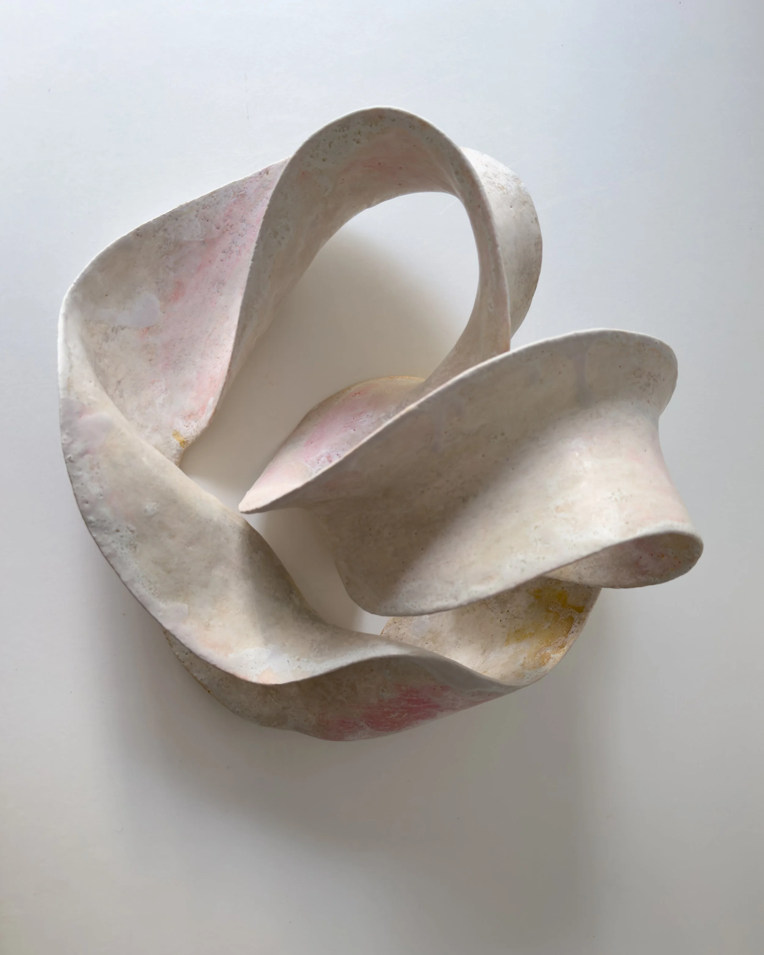 Abstract ceramic sculpture with smooth, flowing curves on a white background.