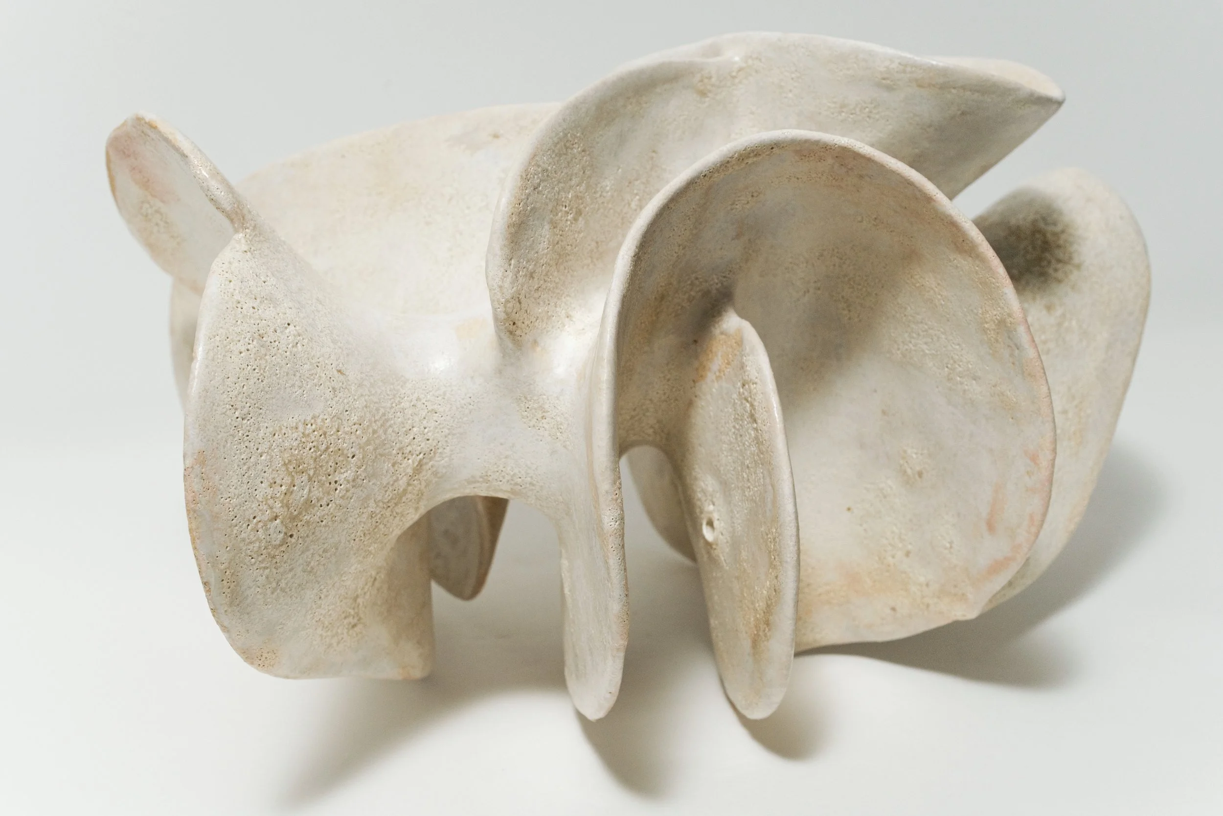 A close-up of an abstract ceramic sculpture with curved, overlapping shapes in a light cream color.