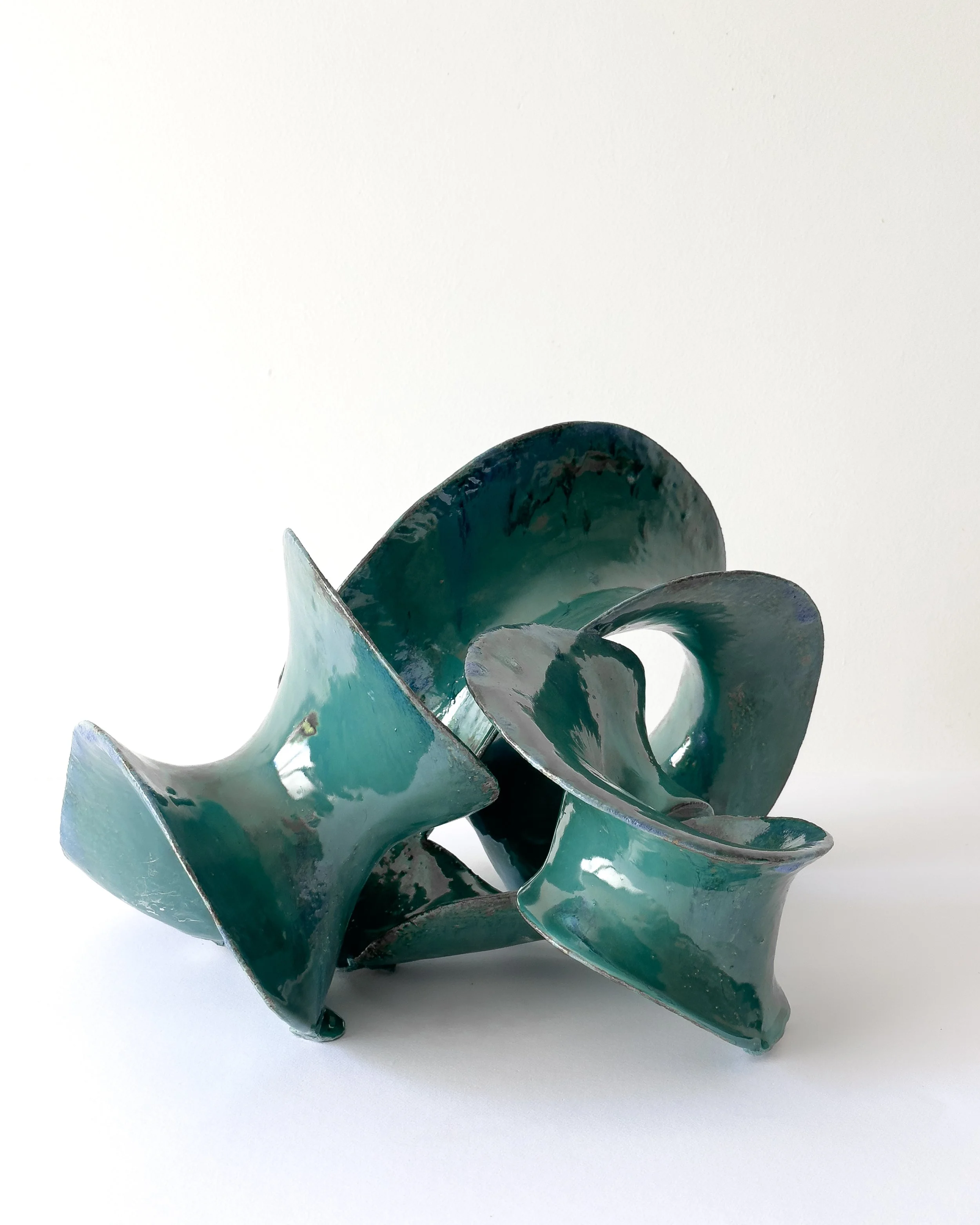 Abstract ceramic sculpture with twisting, ribbon-like shapes in shades of teal and dark green.