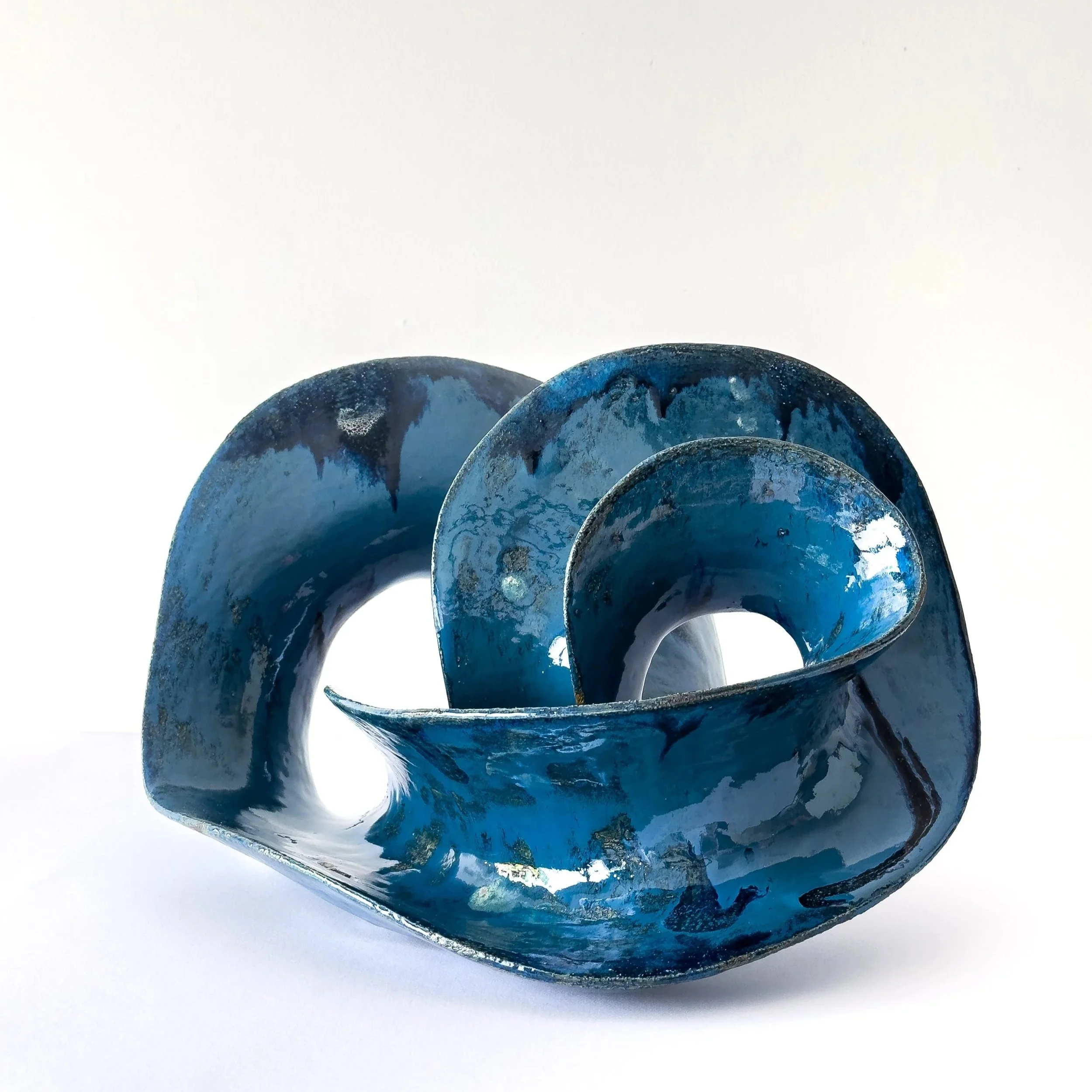 Blue abstract ceramic sculpture with a twisted, looped, and curled form on a white background.