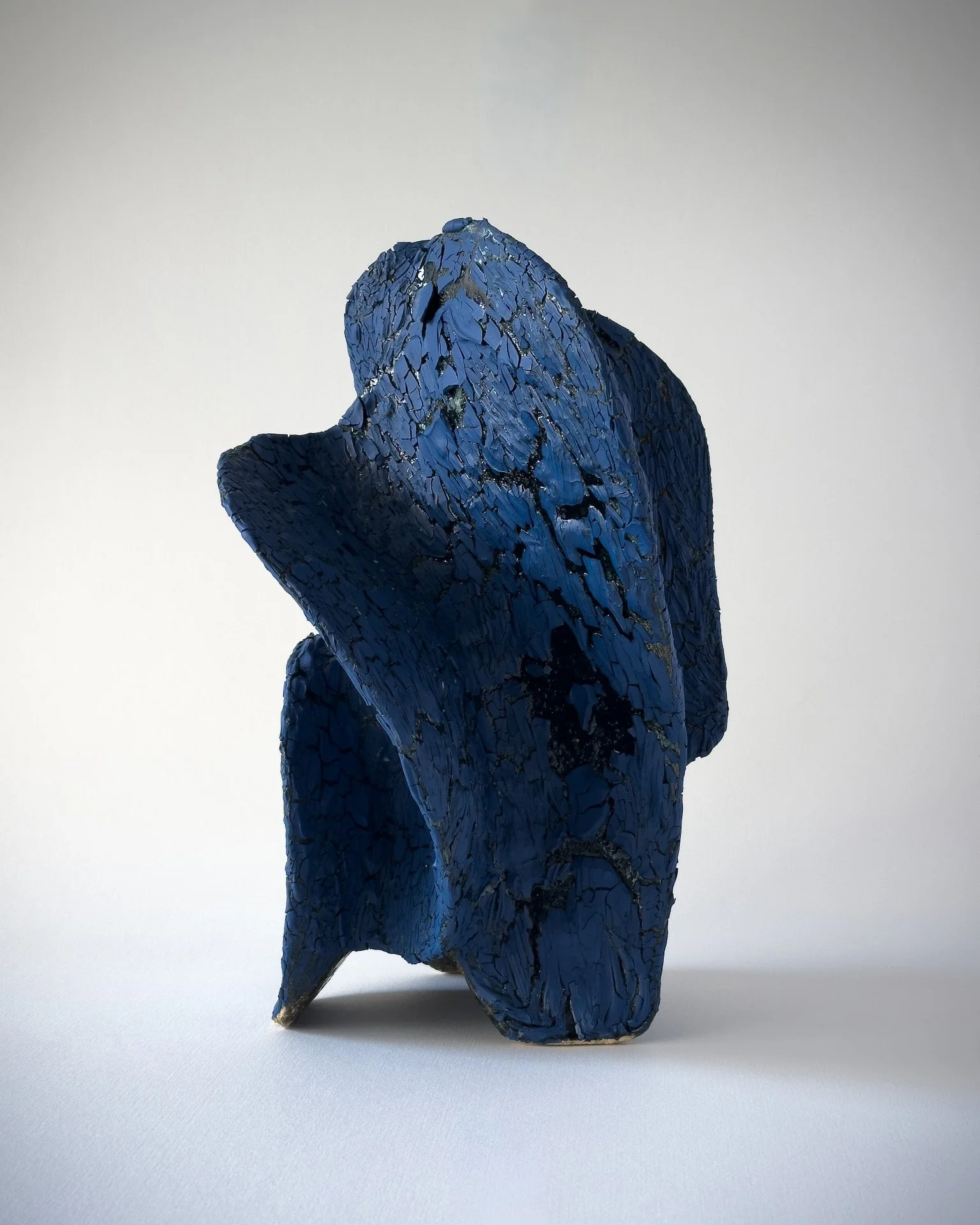 Blue abstract sculpture with a textured, cracked surface, displayed against a plain light background.