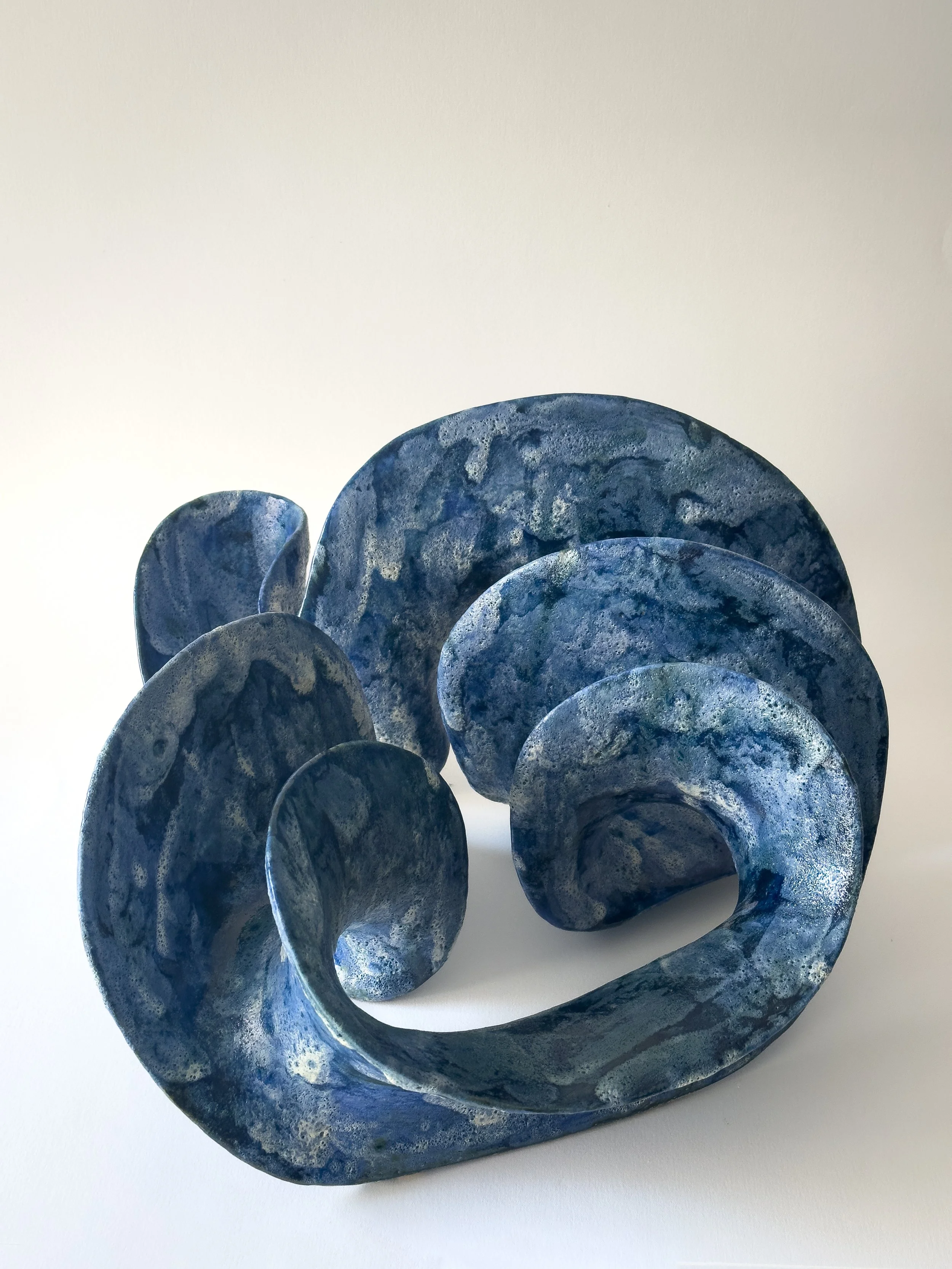 Blue and gray marbled spiral sculpture on a white surface against a white background.