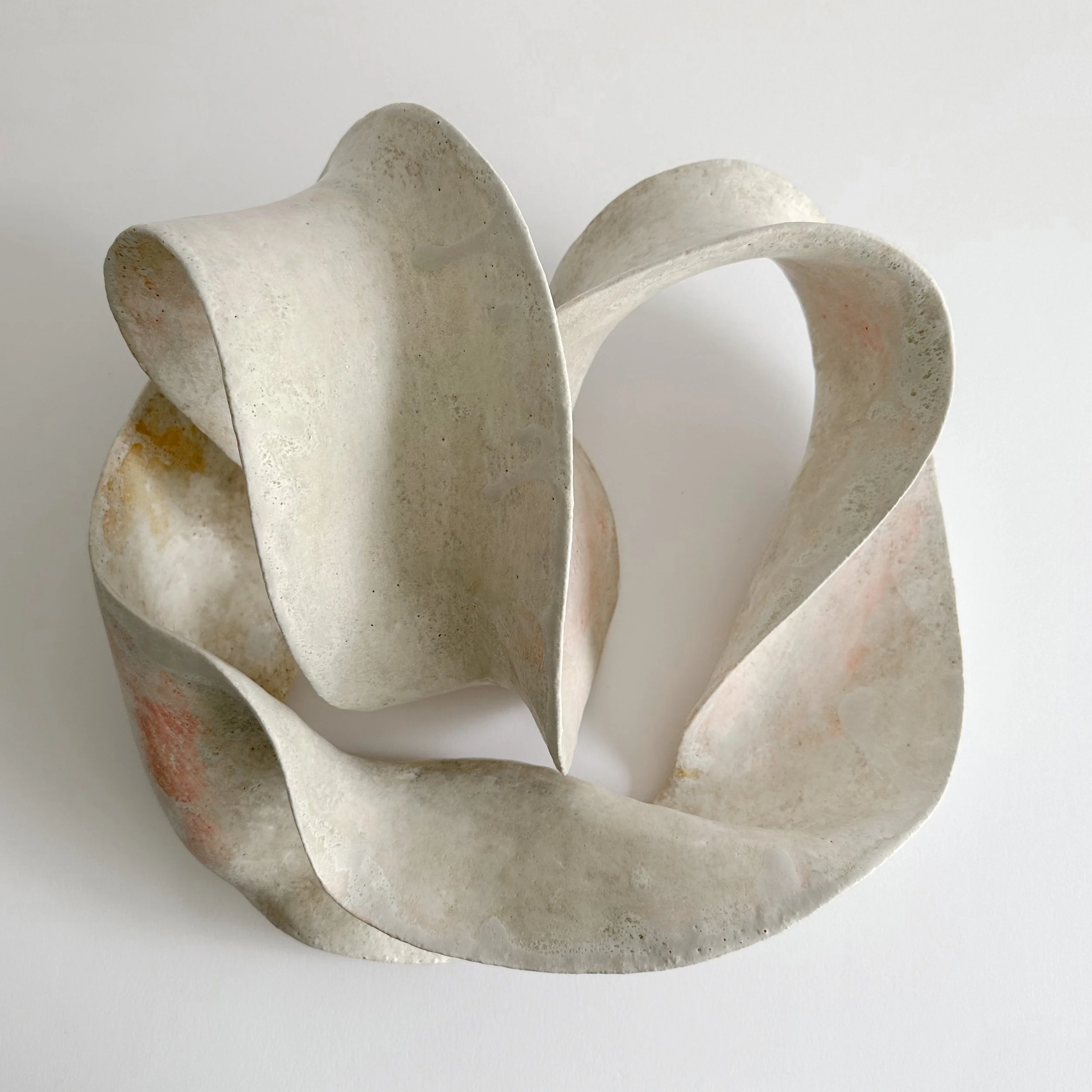 A sculpture made of interconnected, curved, beige and light pinkish stone or ceramic material, arranged in an abstract, flowing form.
