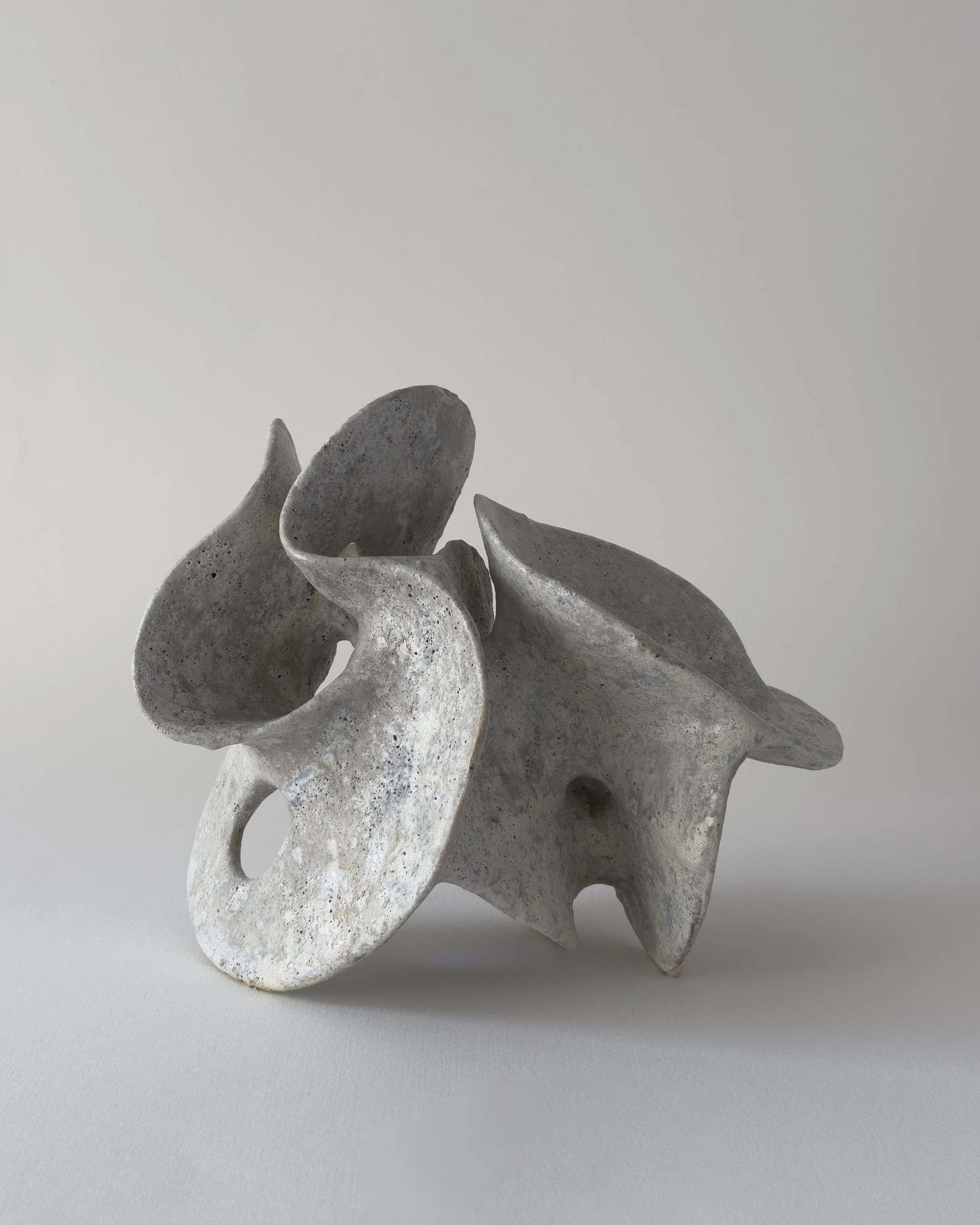 Abstract ceramic sculpture with irregular shapes and holes on a plain white background.