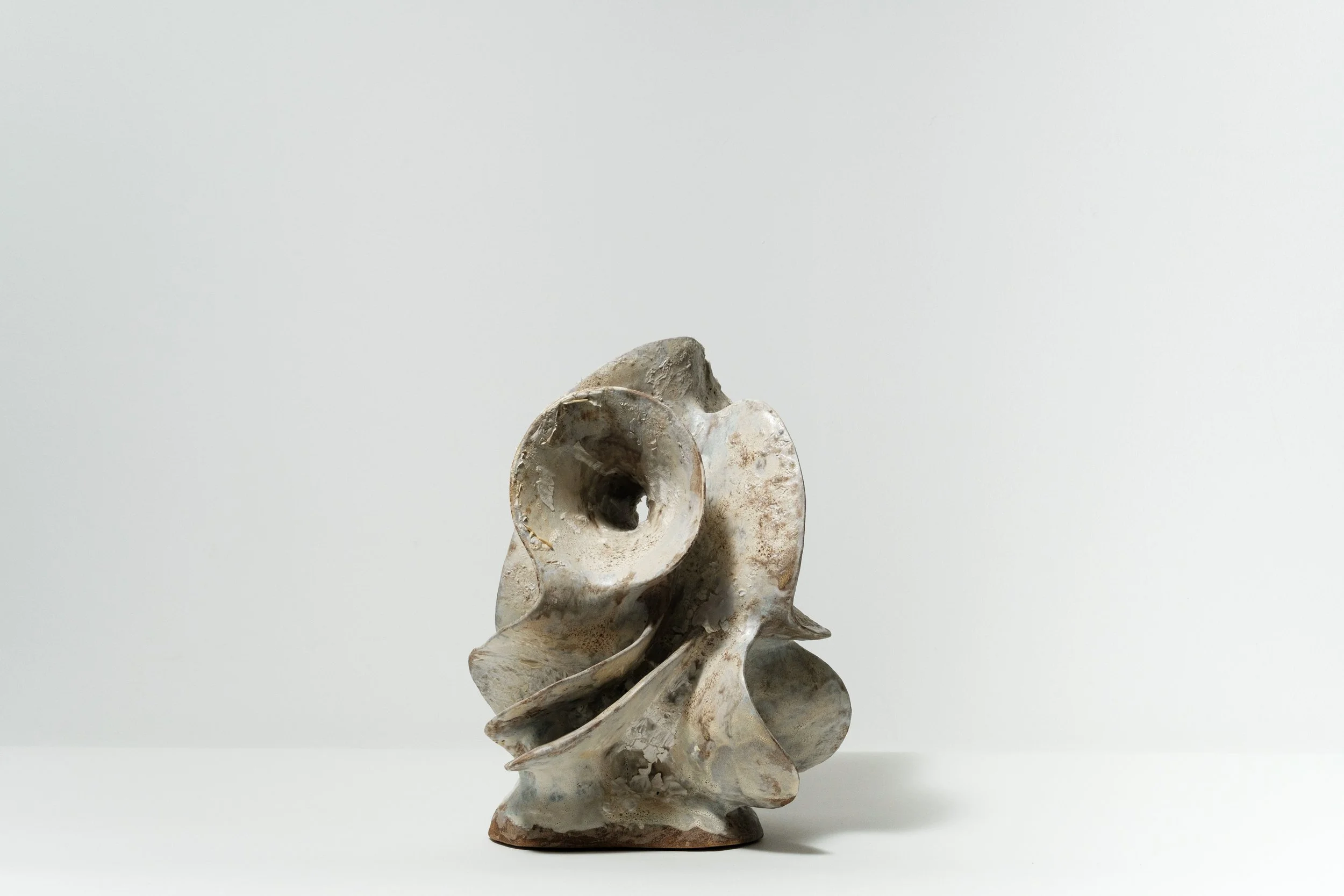 Abstract ceramic sculpture with swirling shapes on a white surface and white background.