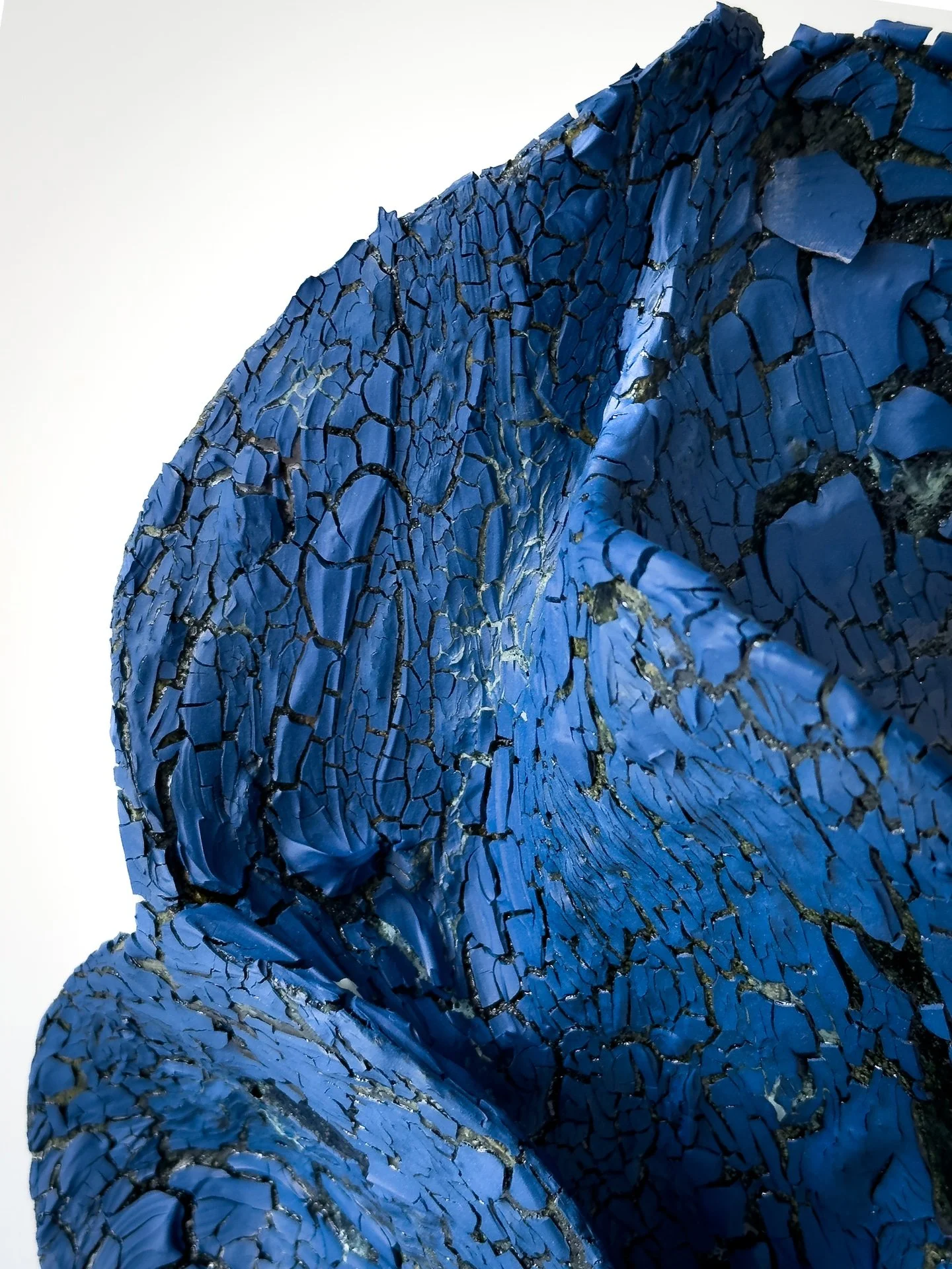 Close-up of a blue, cracked, textured sculpture or artwork with black and gold accents.