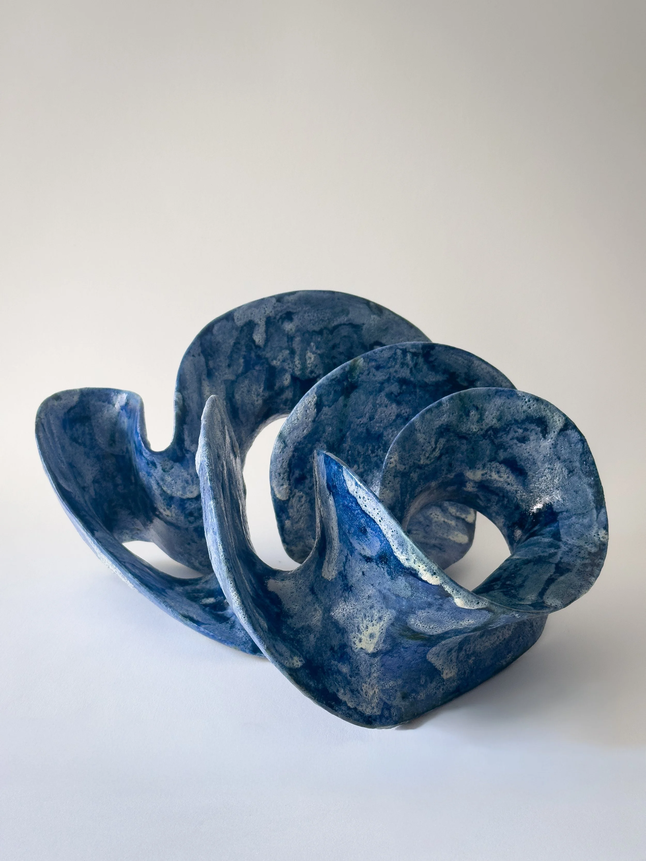 Blue marbled ceramic sculpture with intertwined loops on a white background.