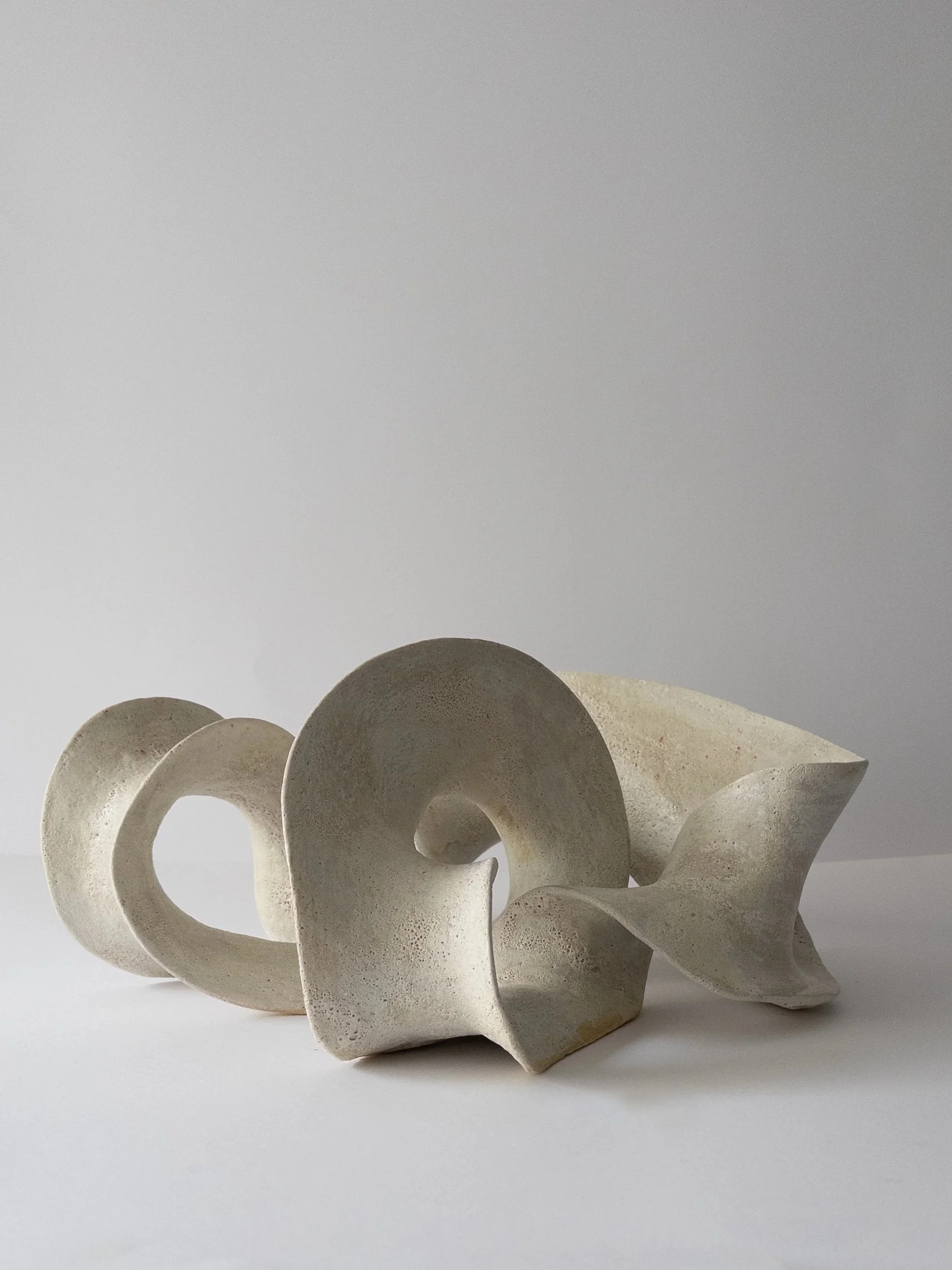 Abstract sculpture with spiral and wave shapes, made of light-colored material against a plain background.
