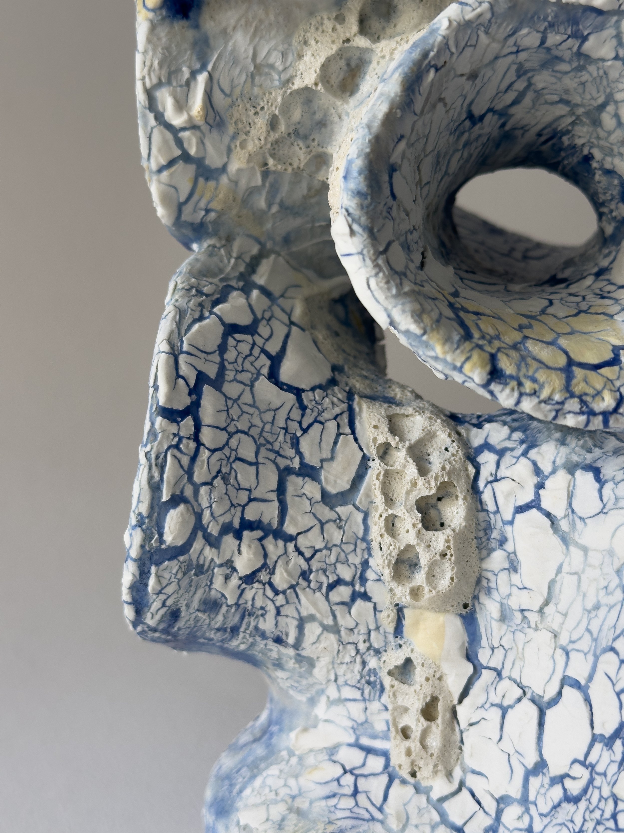 Close-up of a textured ceramic sculpture with a crackled blue and white glaze, featuring a hollow circular opening.