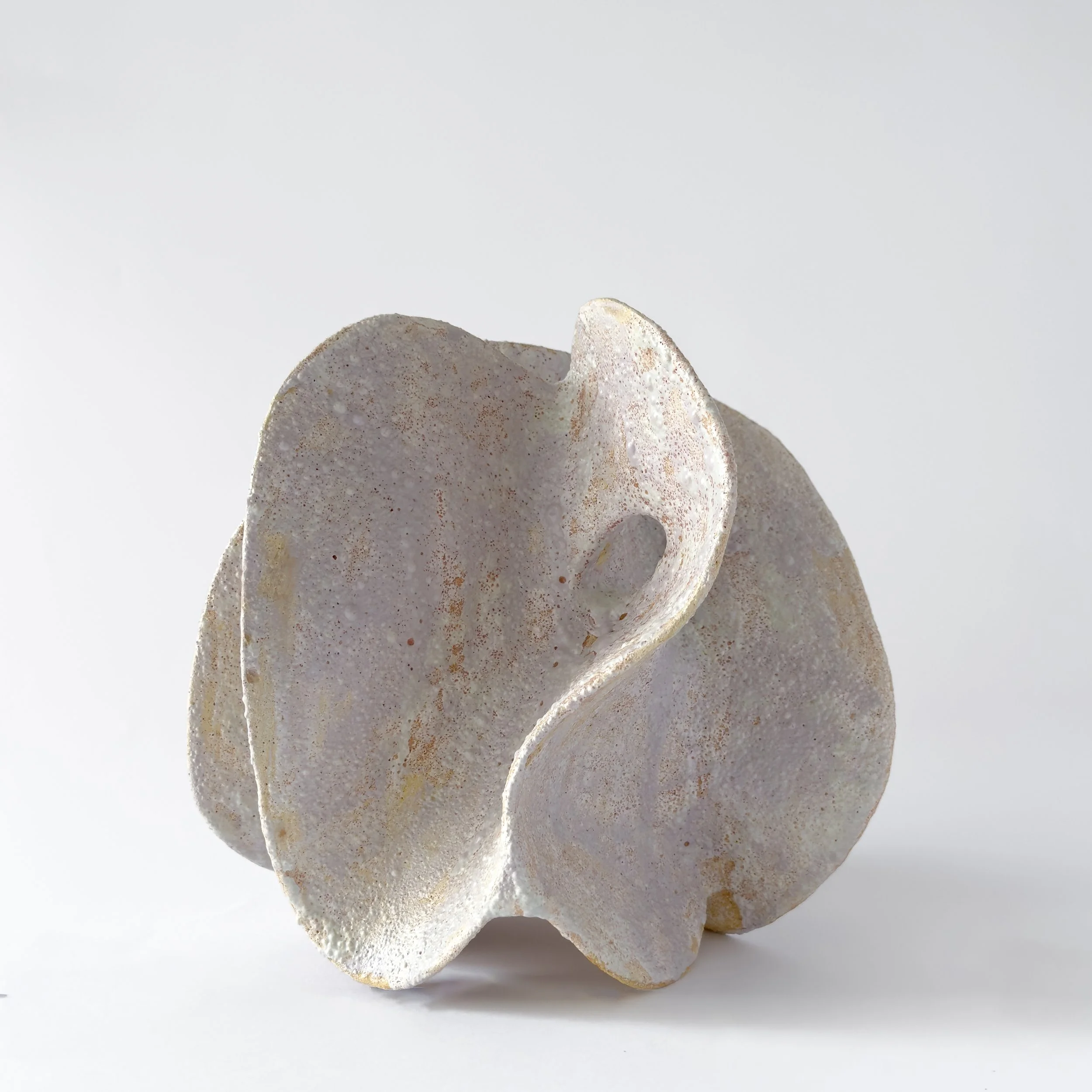 A white, textured ceramic sculpture with abstract, flowing shapes and smooth curves, set against a plain light background.