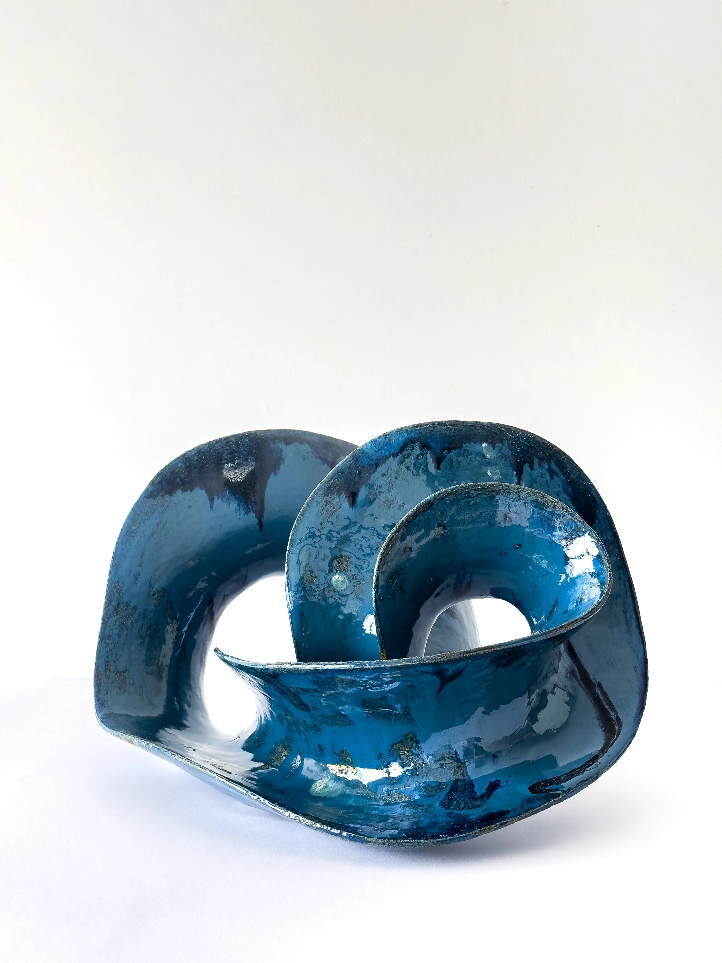 Blue abstract ceramic sculpture with curved forms on a white background.