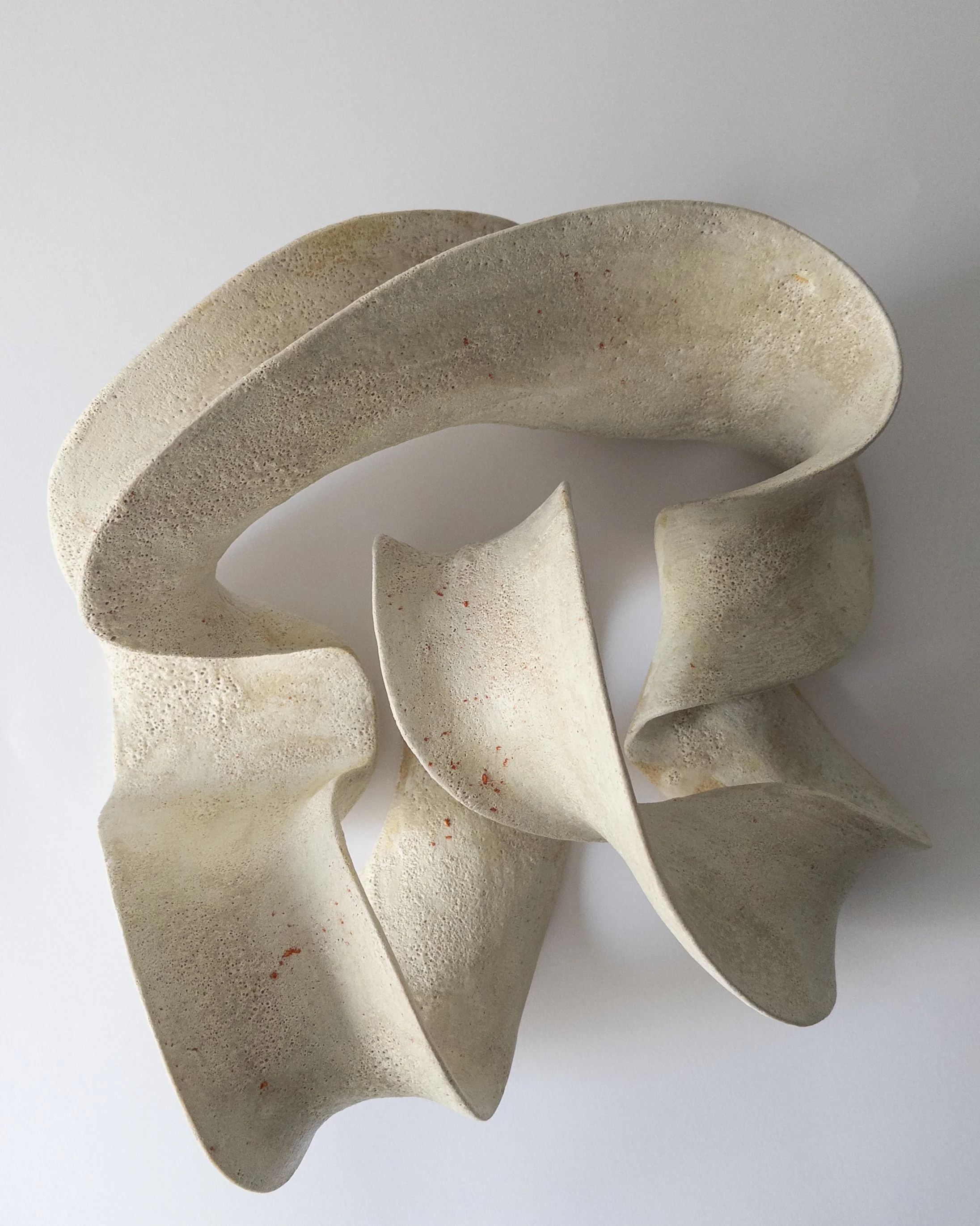 Abstract beige ceramic sculpture with curving, twisting shapes on a white background.