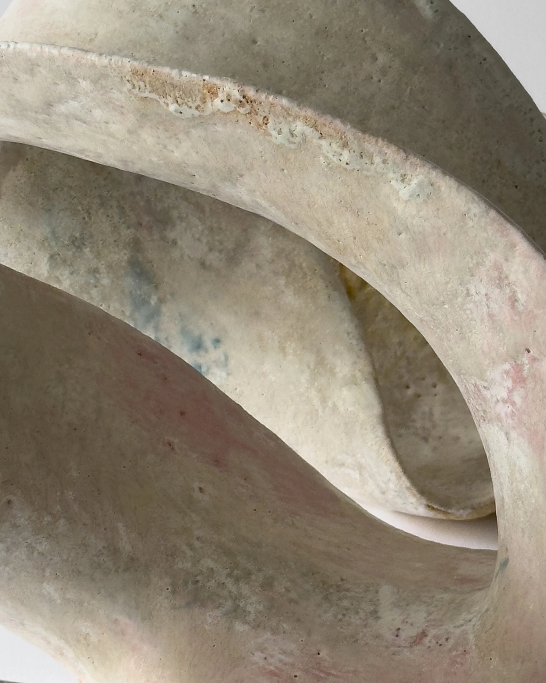 Close-up of a coiled, weathered beige ceramic or clay object with rough, uneven surface and some discoloration.