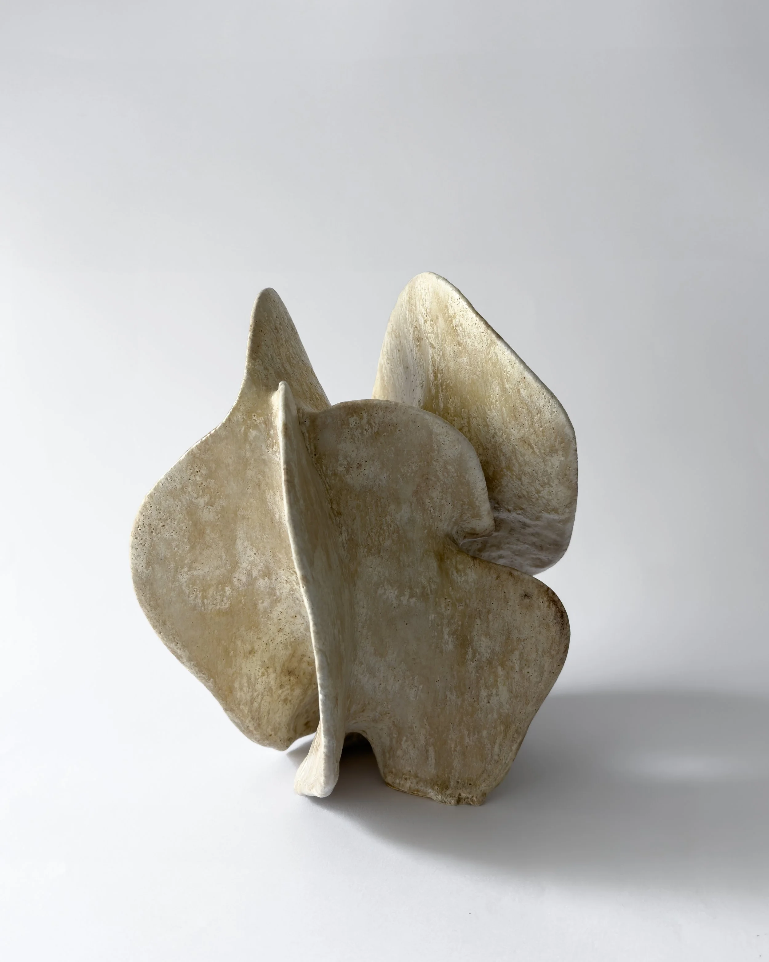 An abstract sculpture made of textured, earthy-toned material with multiple curved, overlapping shapes.