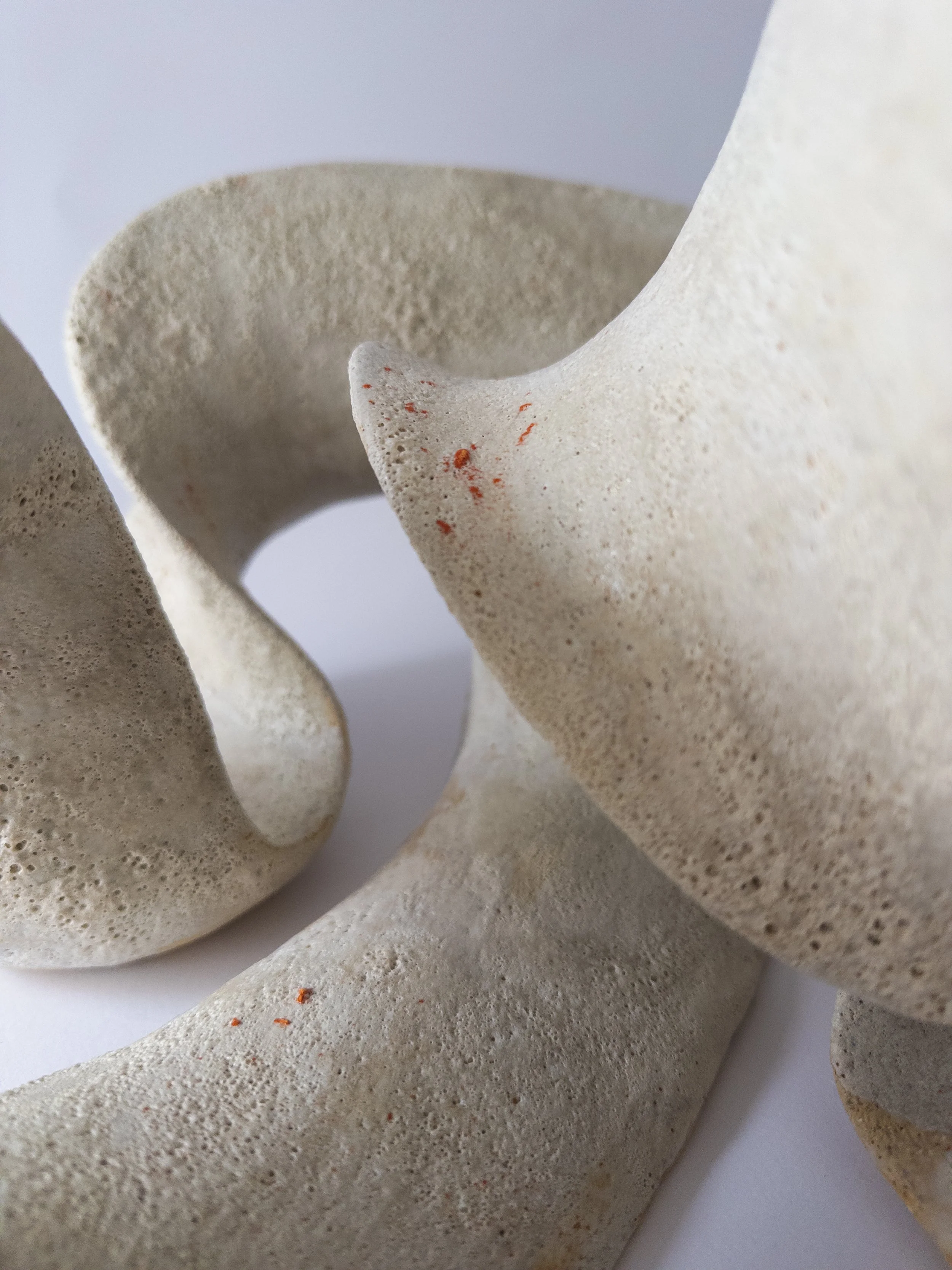 Close-up of abstract beige ceramic sculptures with smooth, curving, organic shapes on a white background.