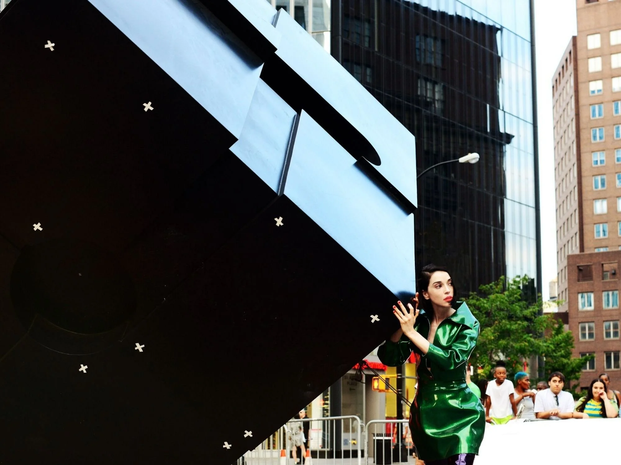 A performer in a metallic green jacket stands beside a large geometric sculpture in an urban setting during the filming of a stylized music video, showcasing the creative direction of a music video production Philadelphia team.