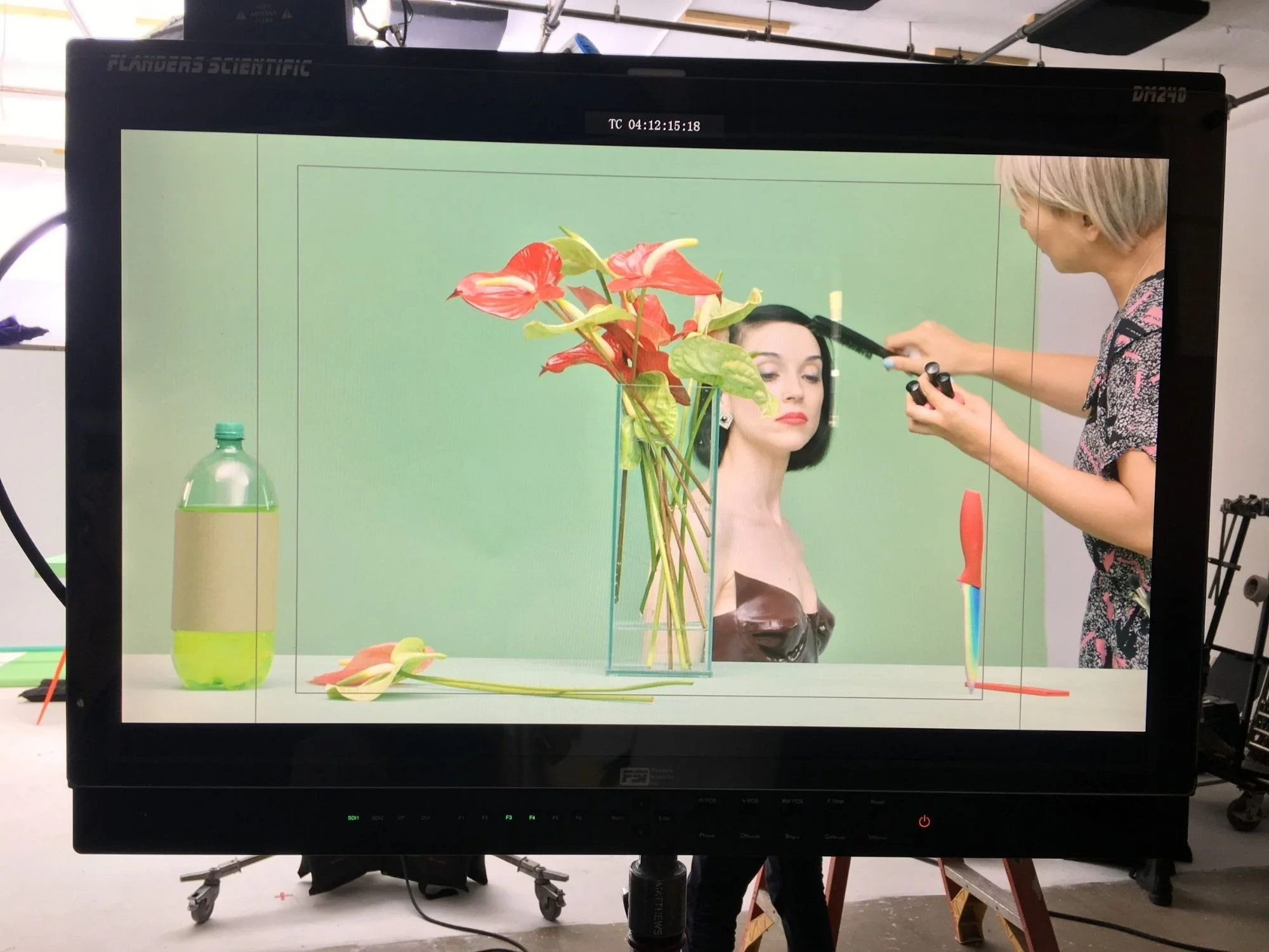 A stylist makes final touch-ups to a performer on a colorful studio set while the scene is viewed through a production monitor, showcasing the creative process behind music production Philadelphia and music video production Philadelphia.