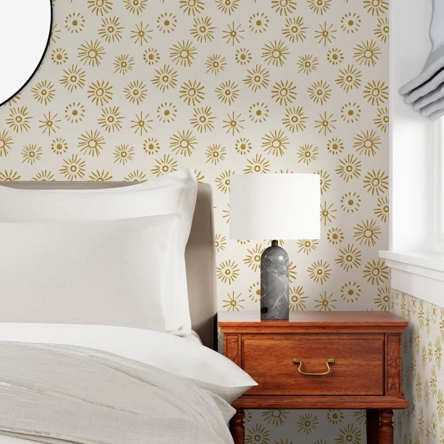 A bedroom corner with a bed, wooden nightstand, and a marble-based table lamp on top, with gold and white patterned wallpaper in the background.