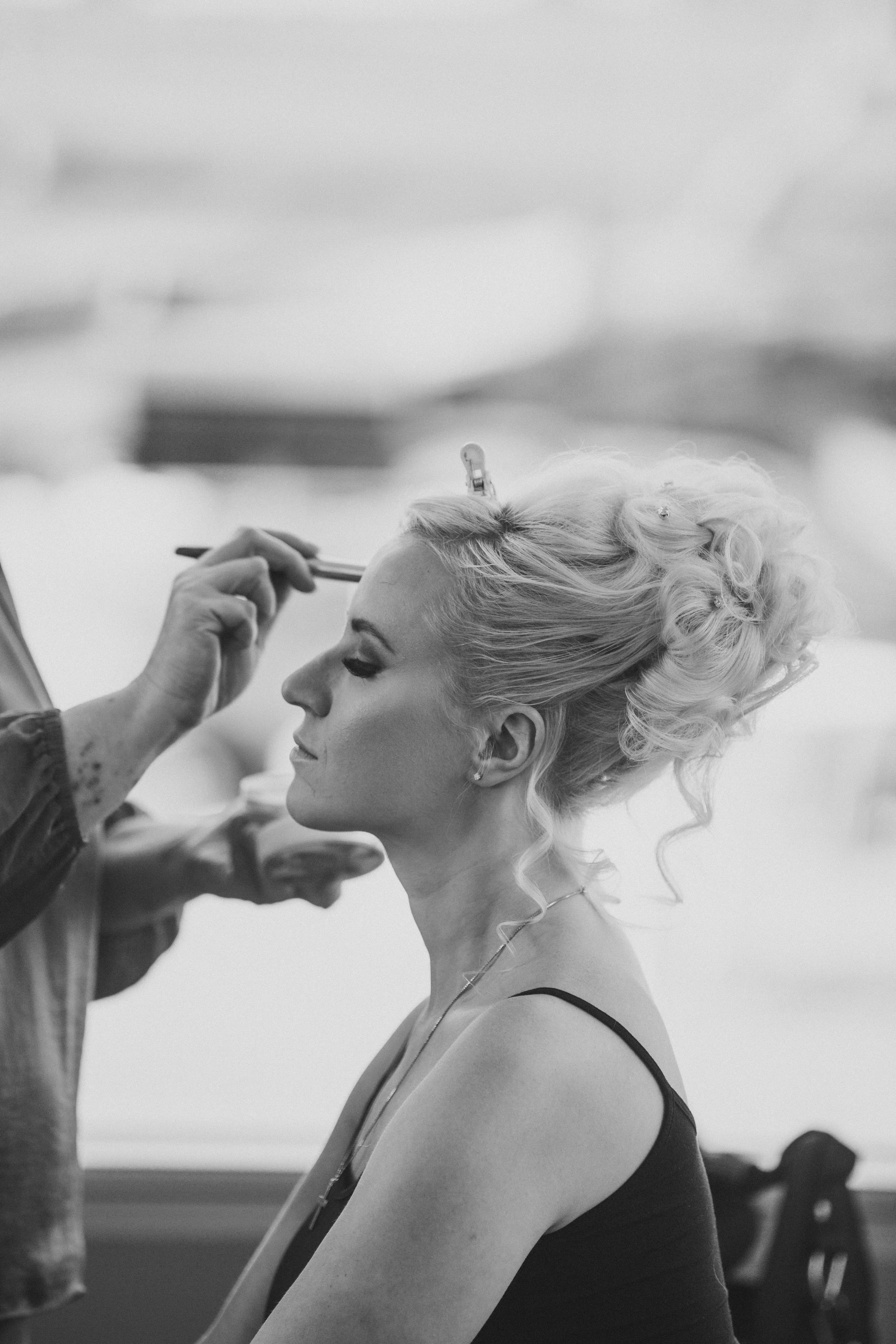 A woman with an elegant updo hairstyle getting makeup applied by a makeup artist in a photography setting.