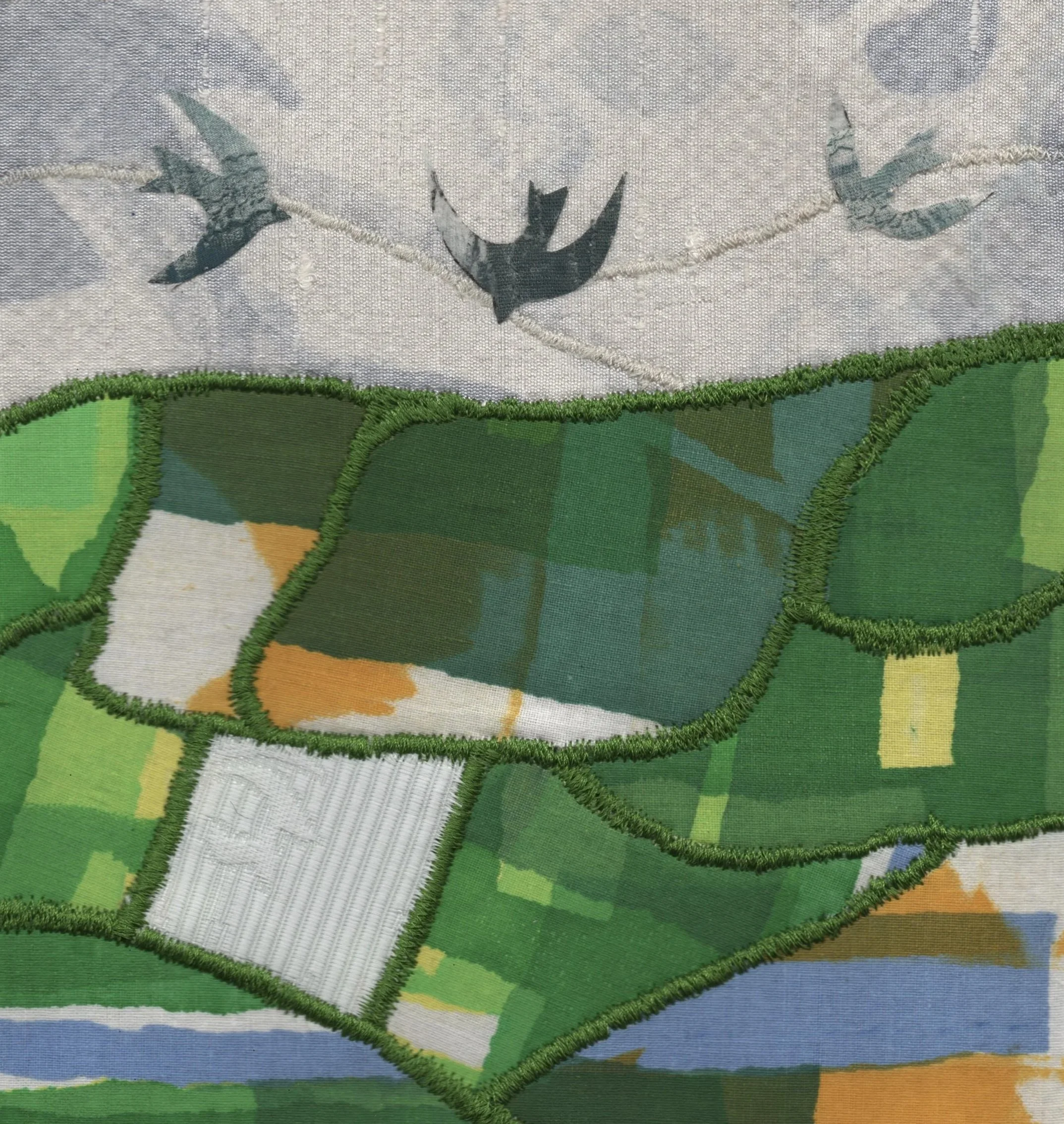 Close-up view of embroidered patches with a bird and a green landscape scene, showing detailed stitching and fabric textures.