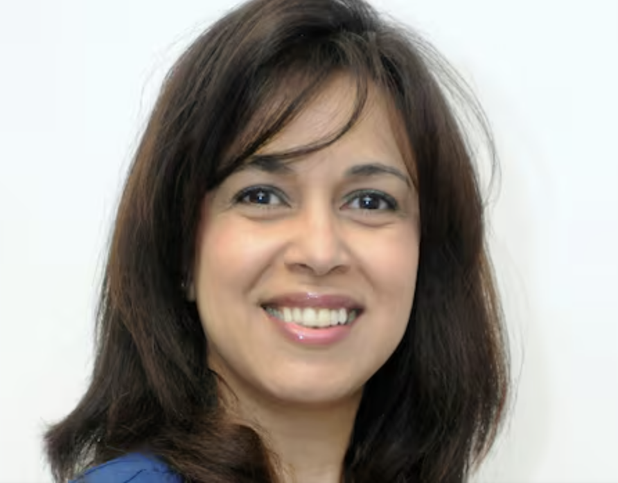 Close-up of a smiling woman with shoulder-length brown hair and brown eyes, wearing a blue top, against a white background.