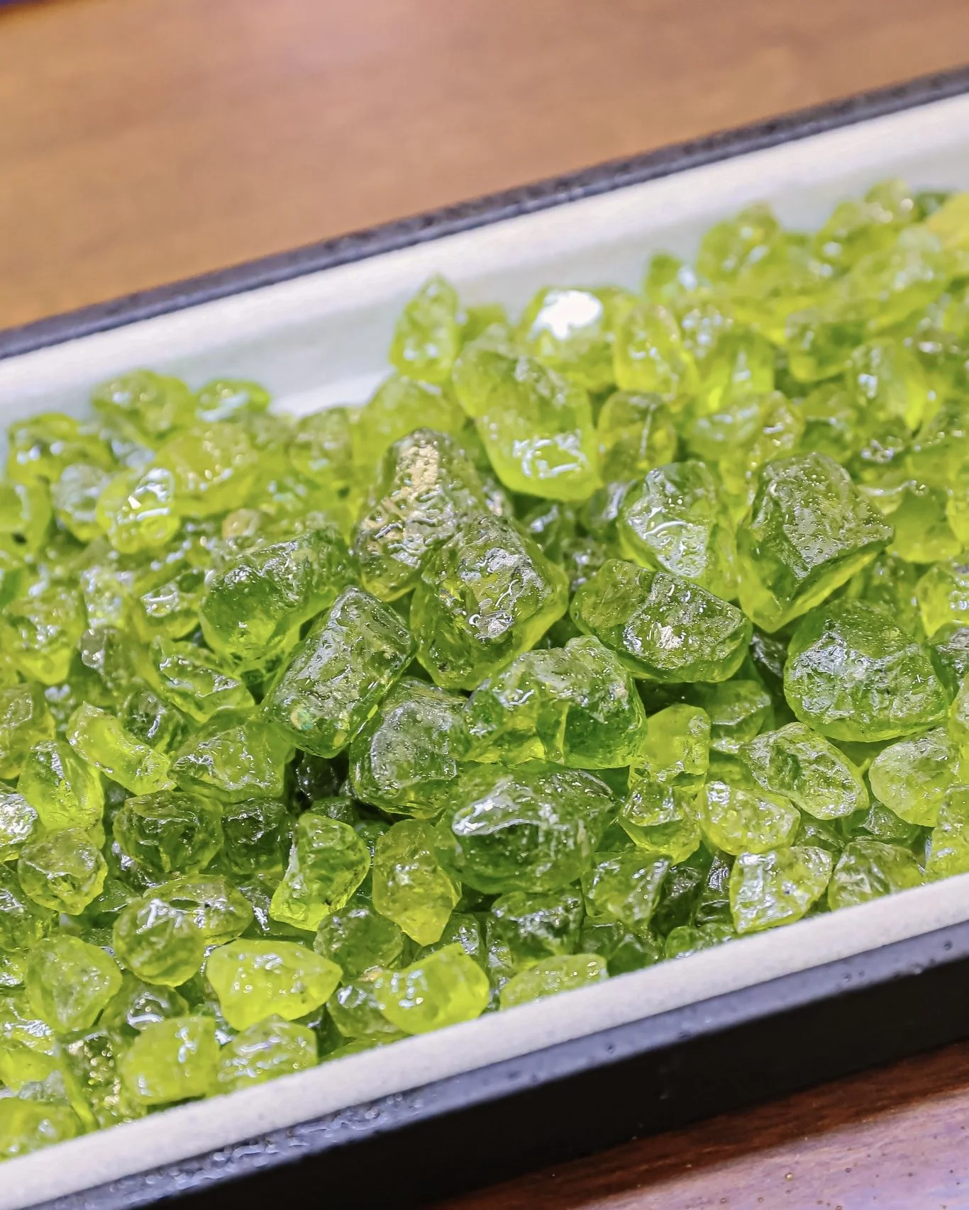 Close-up of green candied ginger pieces on a white and black rectangular tray.