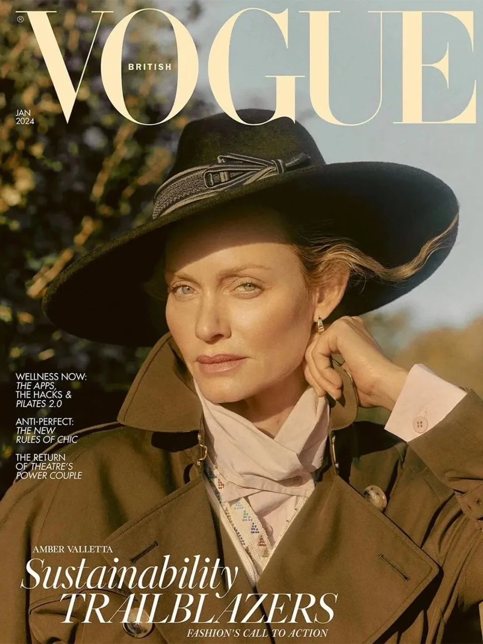 The cover of Vogue British magazine, January 2024 issue, featuring Amber Valletta wearing a large black hat, tan trench coat, and a white scarf, outdoors with a blurred natural background.